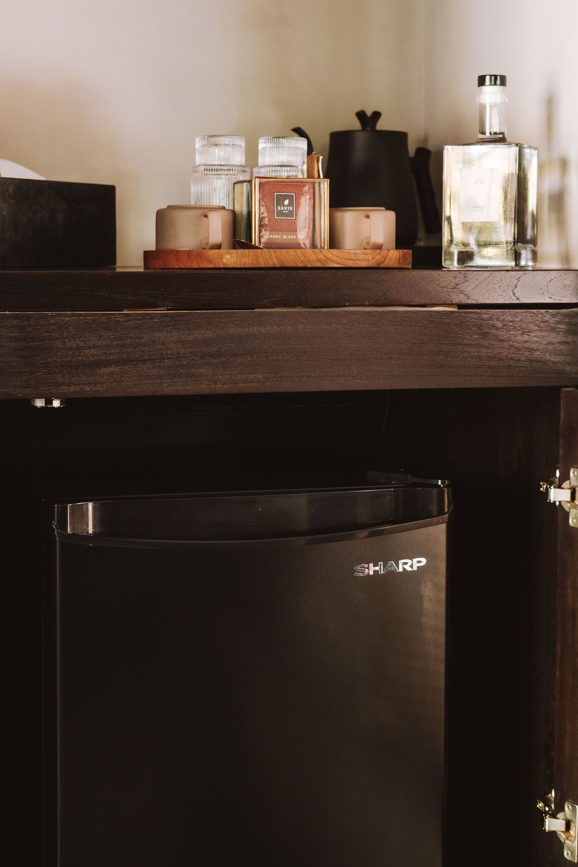 Compact black mini fridge beneath a wooden shelf with bottles and toiletries on top