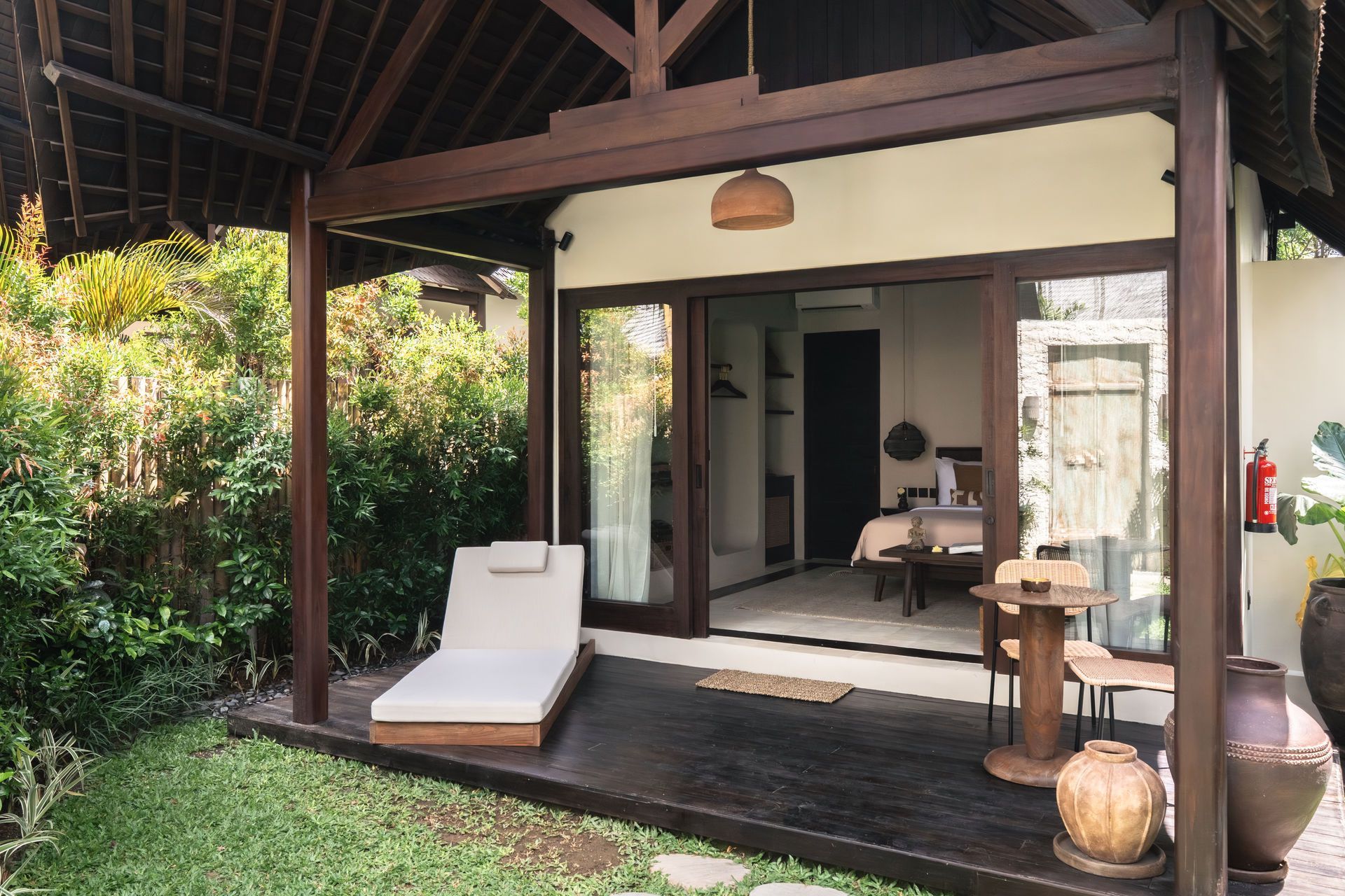 Thatched patio with lounge chair, open sliding doors, and greenery around a tropical villa patio
