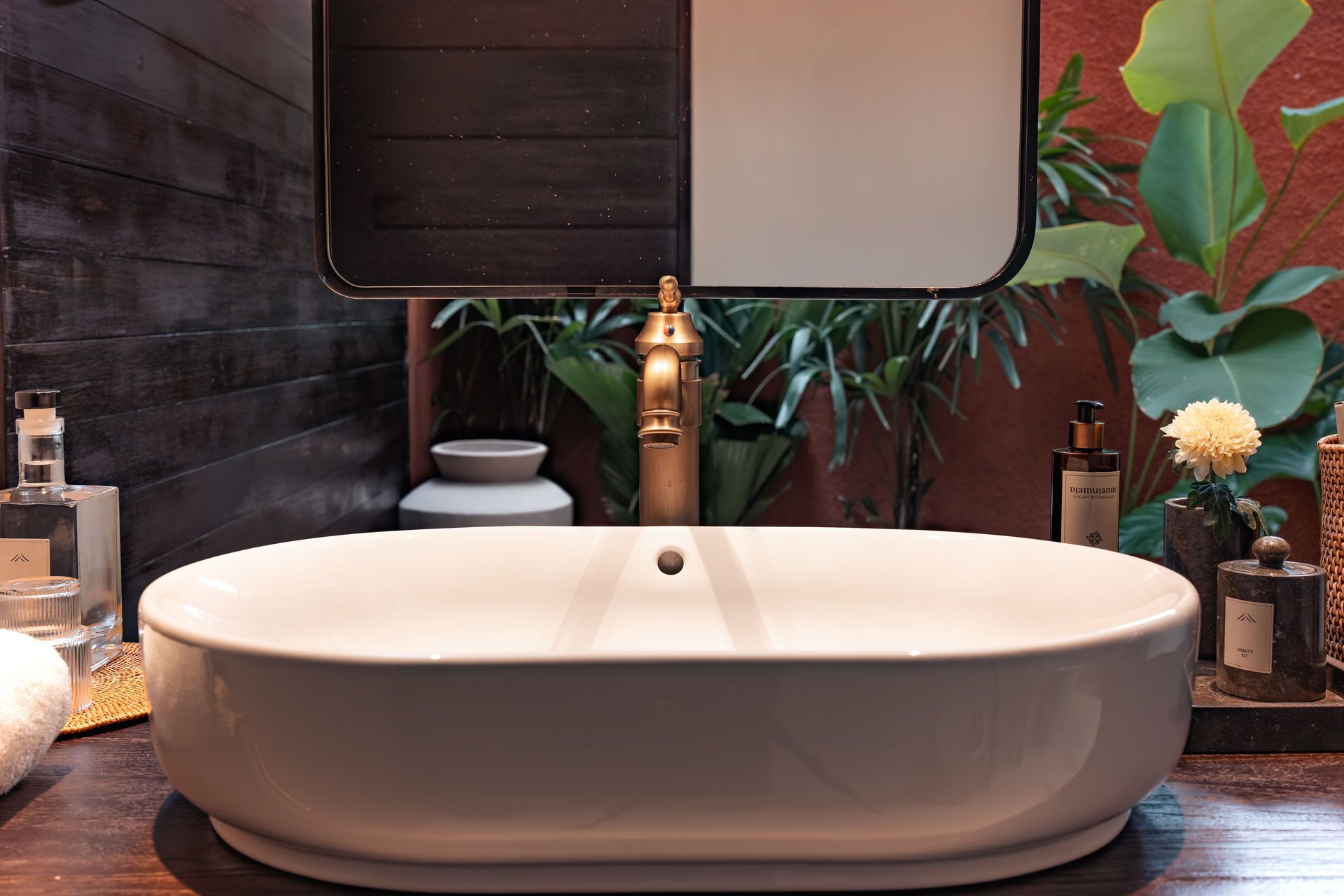 Modern bathroom vanity with white vessel sink, gold faucet, and mirror above wooden counter