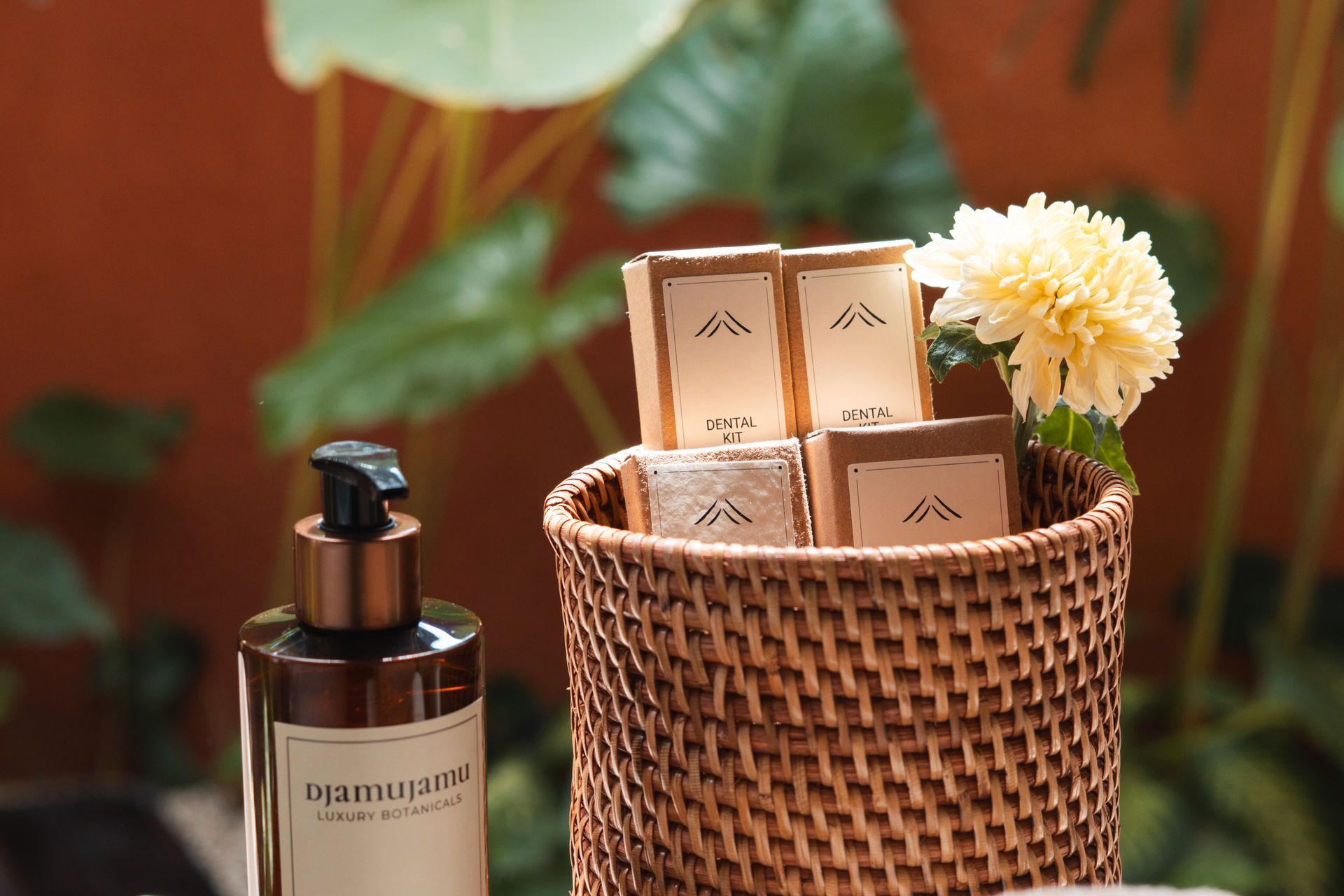 Luxury skincare bottles and boxes in a woven basket beside a flower on a warm-toned table