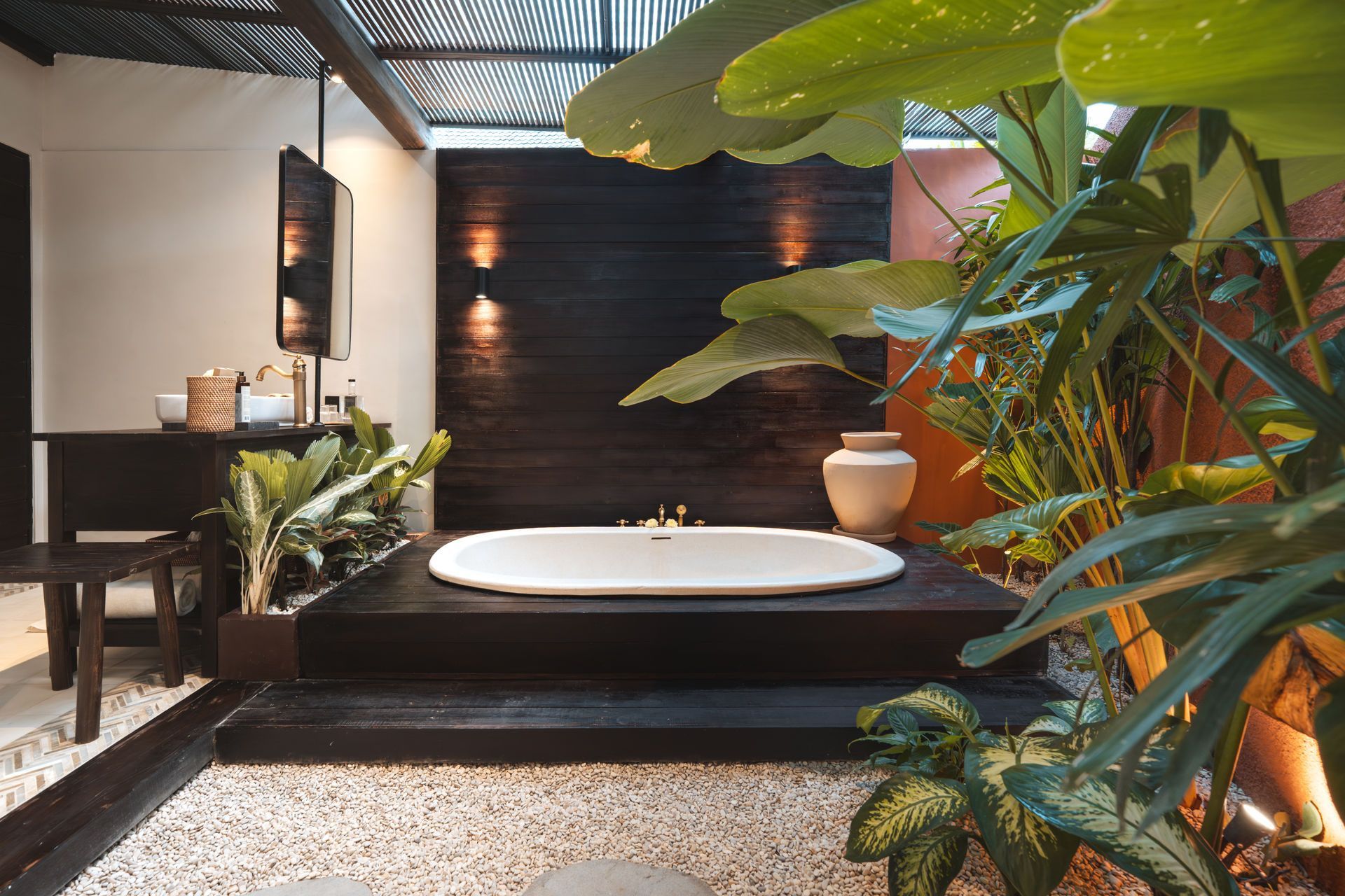 Modern outdoor bathroom with a white tub, black wall, and lush tropical plants