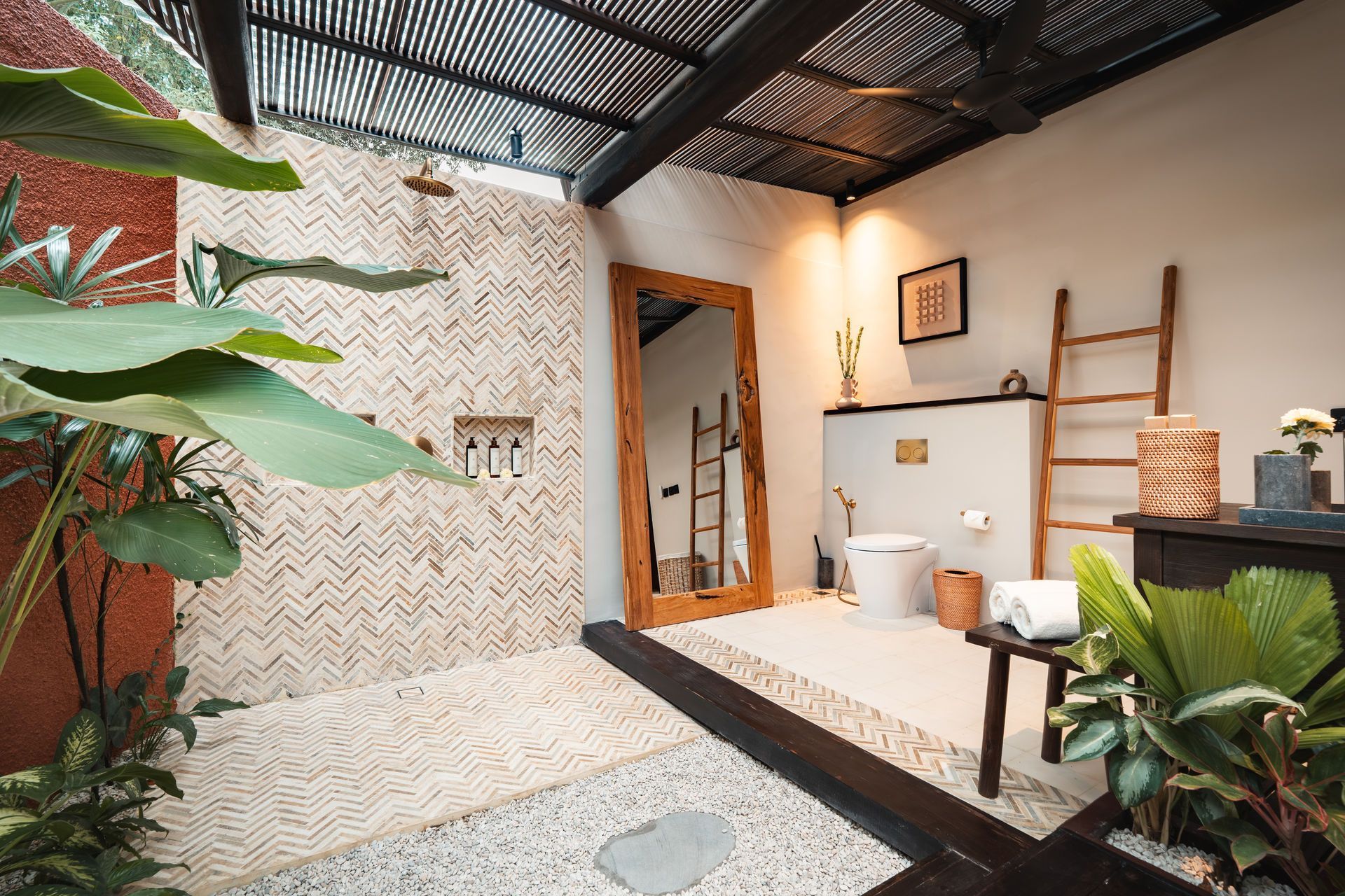Small tiled bathroom with white fixtures, open doorway, and lush potted plants under a dark roof