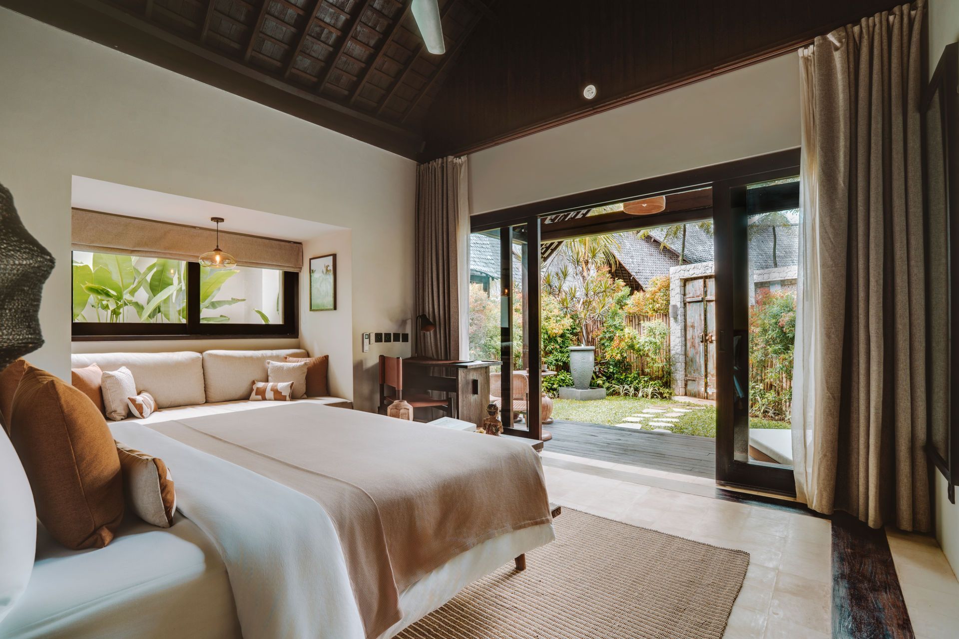 Modern bedroom with a king bed, open glass doors, and a view of a tropical garden