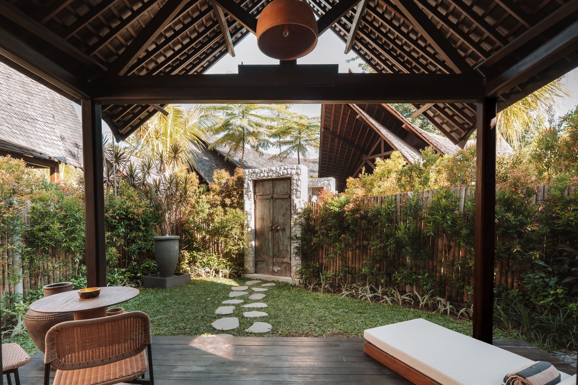 Tropical patio with thatched roof, wicker seating, and stone path leading to a garden gate