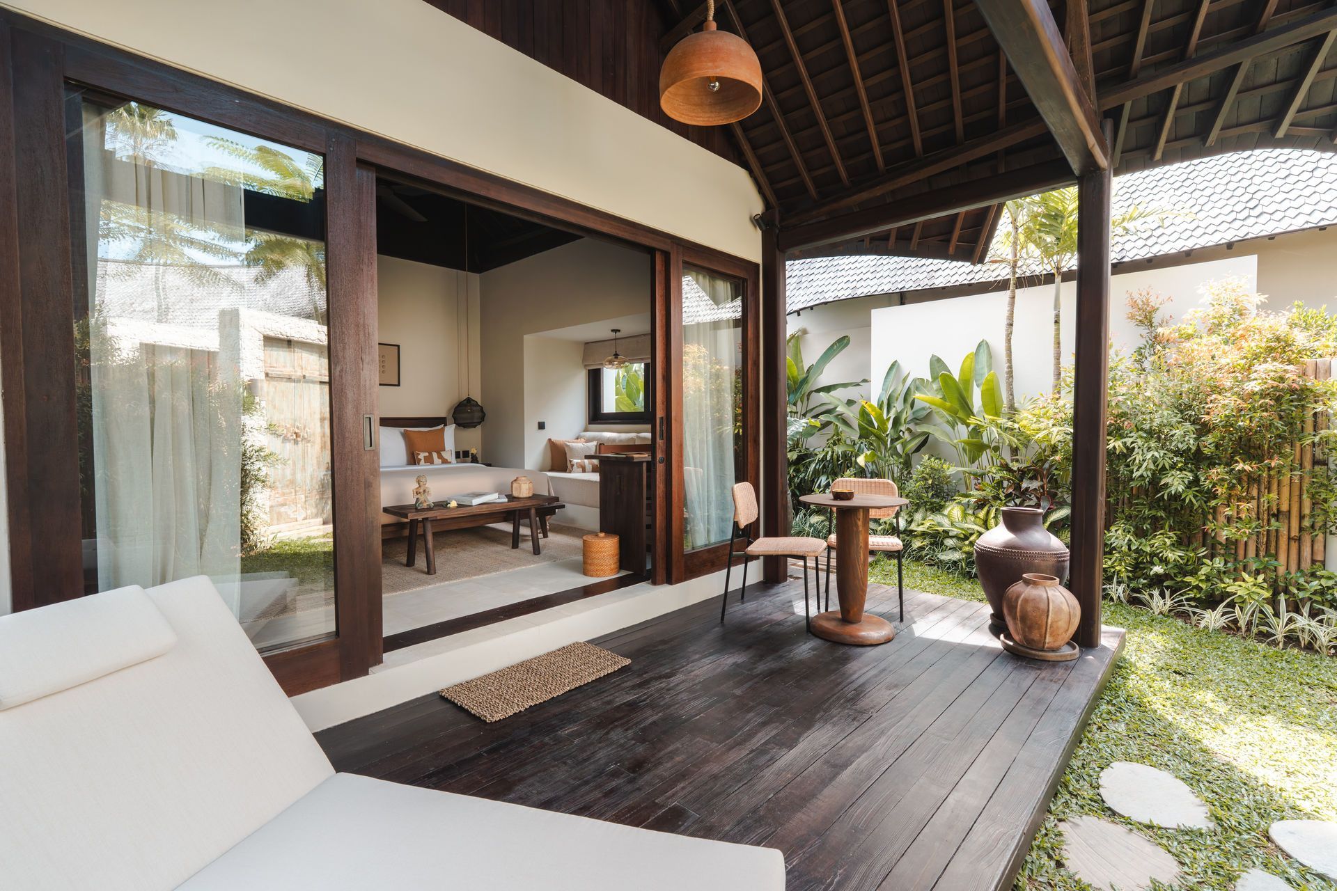 Modern patio with sliding glass doors, lounge chair, dark wood deck, and lush tropical plants