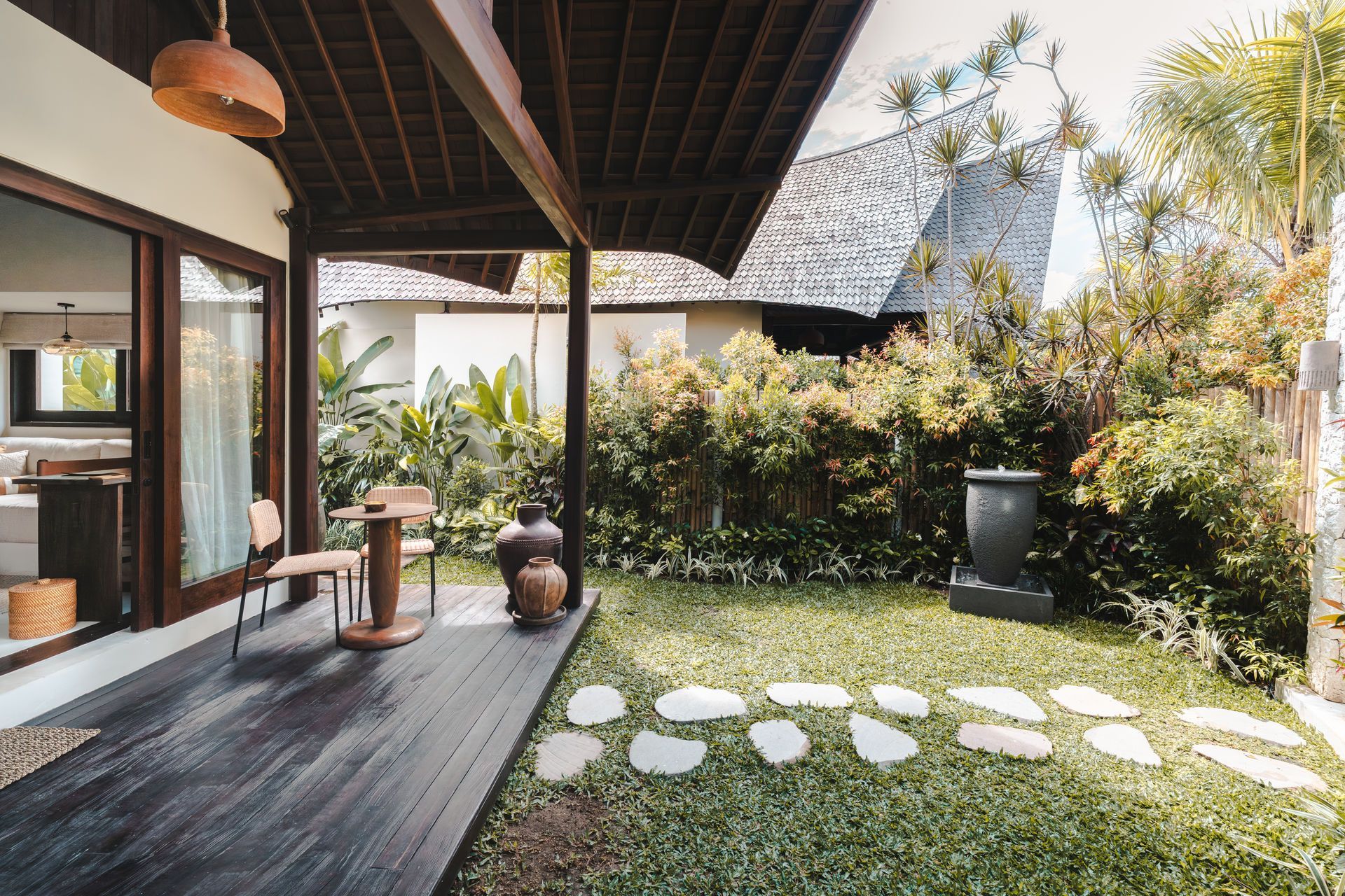 Covered patio with wooden deck, seating, and a lush garden path with round stepping stones