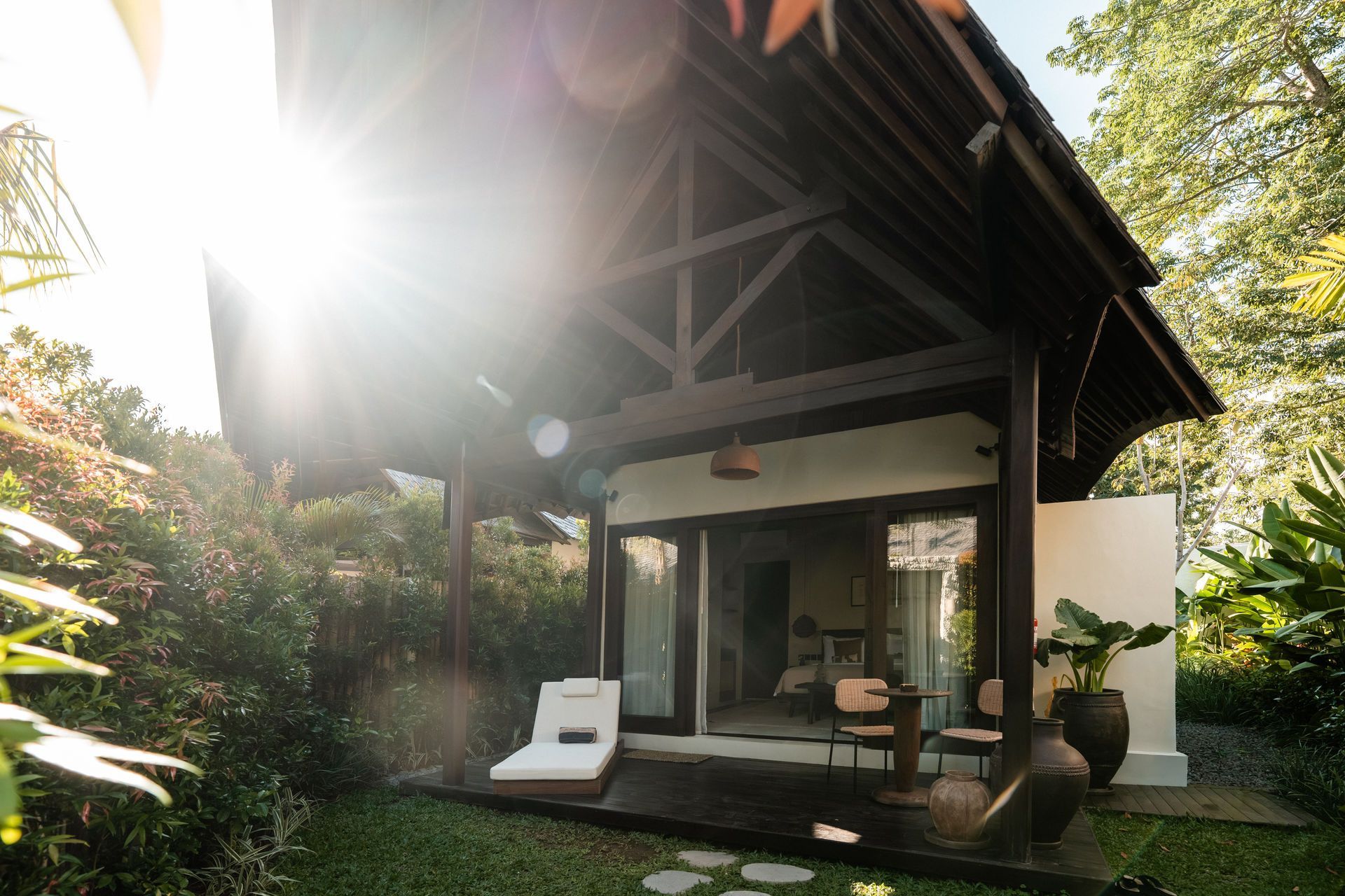 Sunlit tropical patio with a thatched-roof cabana, lounge chair, and lush greenery