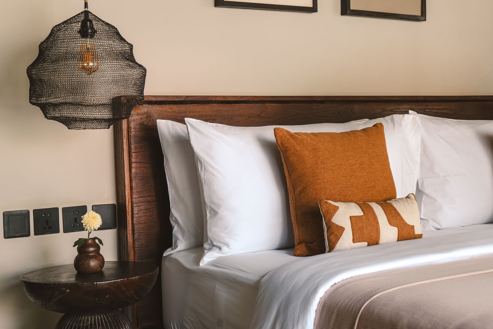 Stylish bedroom with white bedding, rust accent pillows, and a bedside lamp on a wood-paneled headboard