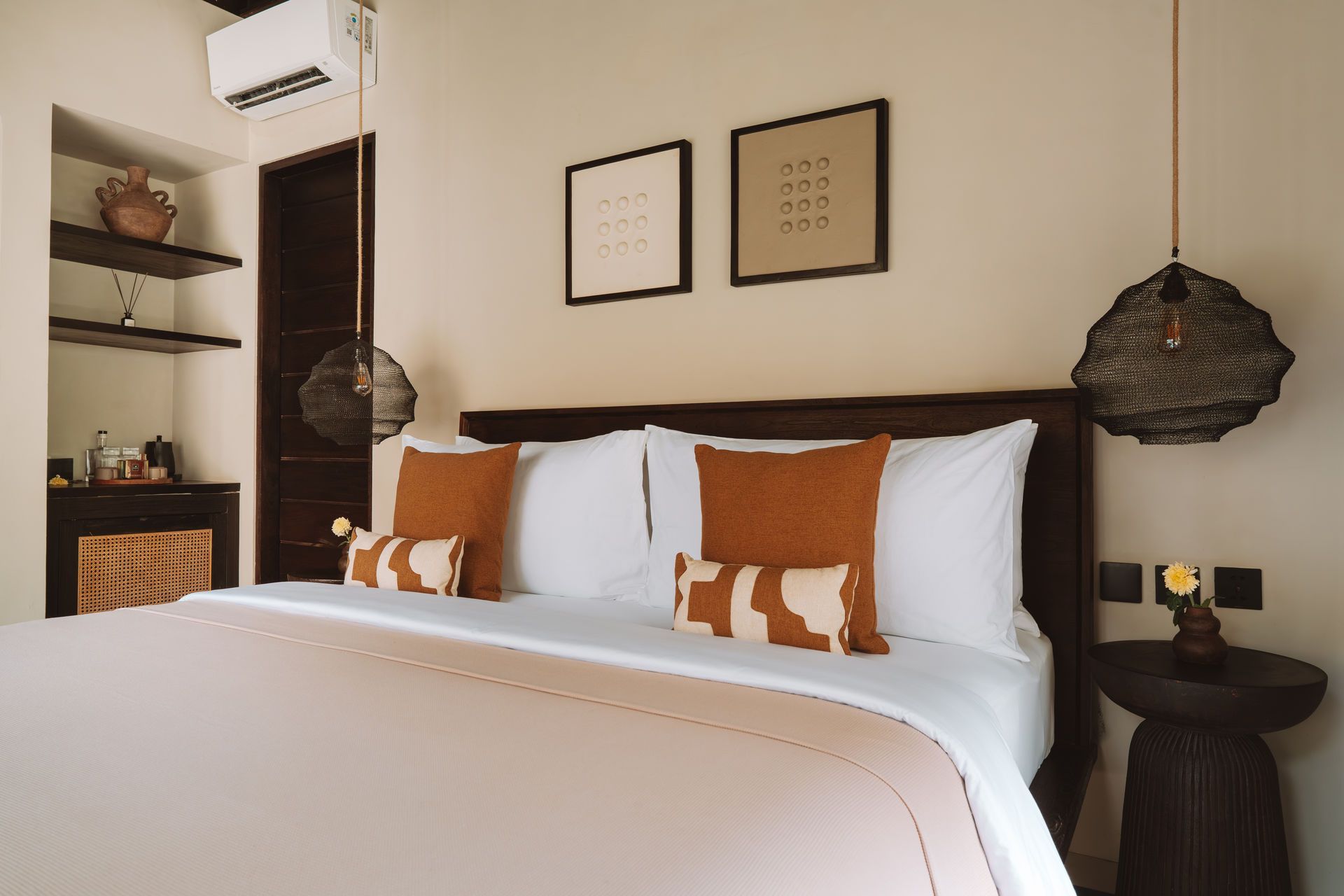 Cozy bedroom with a white bed, rust accents, wall art, shelves, and woven pendant lights