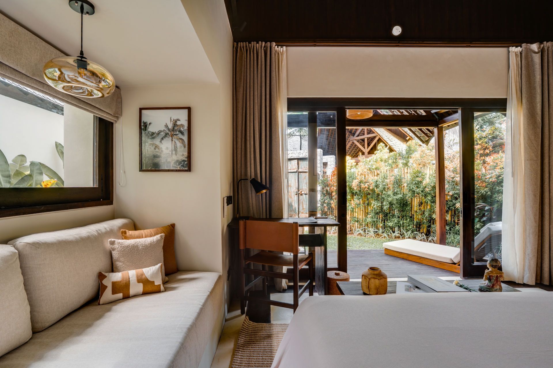Bright, modern bedroom with a bed, sofa, desk, and open sliding doors to a patio and garden.