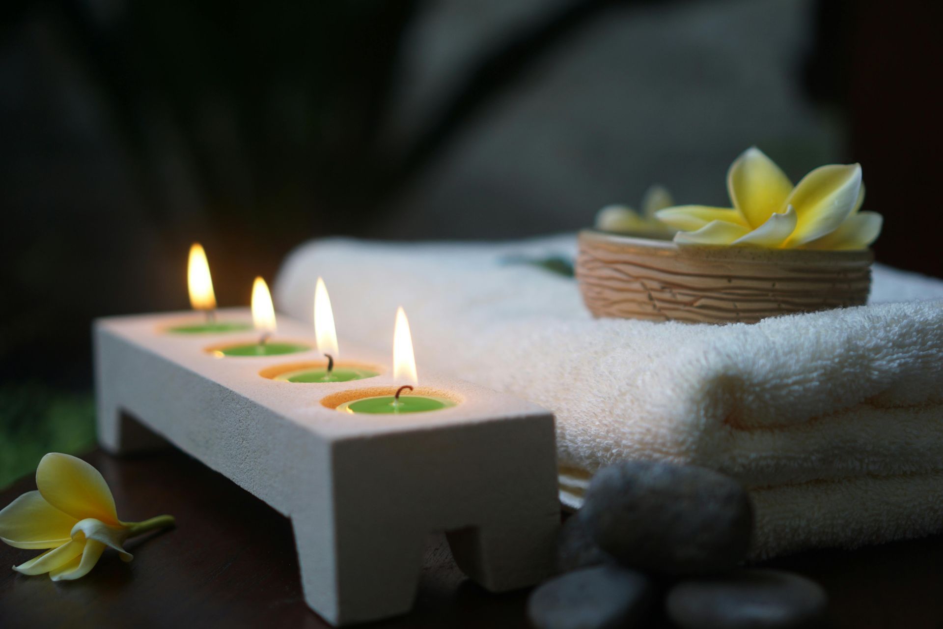Spa candles and yellow flowers beside a folded white towel on smooth stones