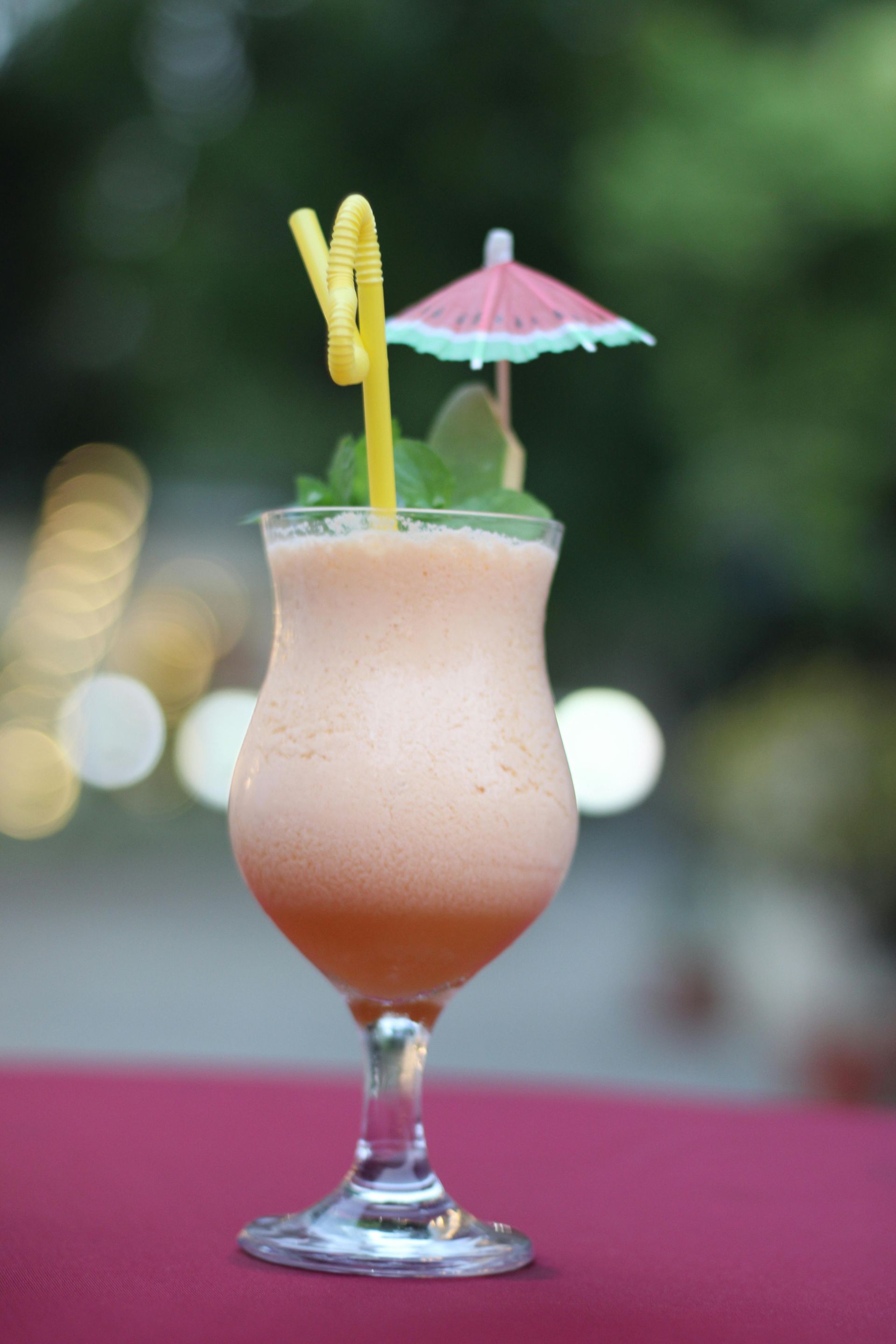 Pink tropical cocktail in a stemmed glass with straw and paper umbrella on a table outdoors