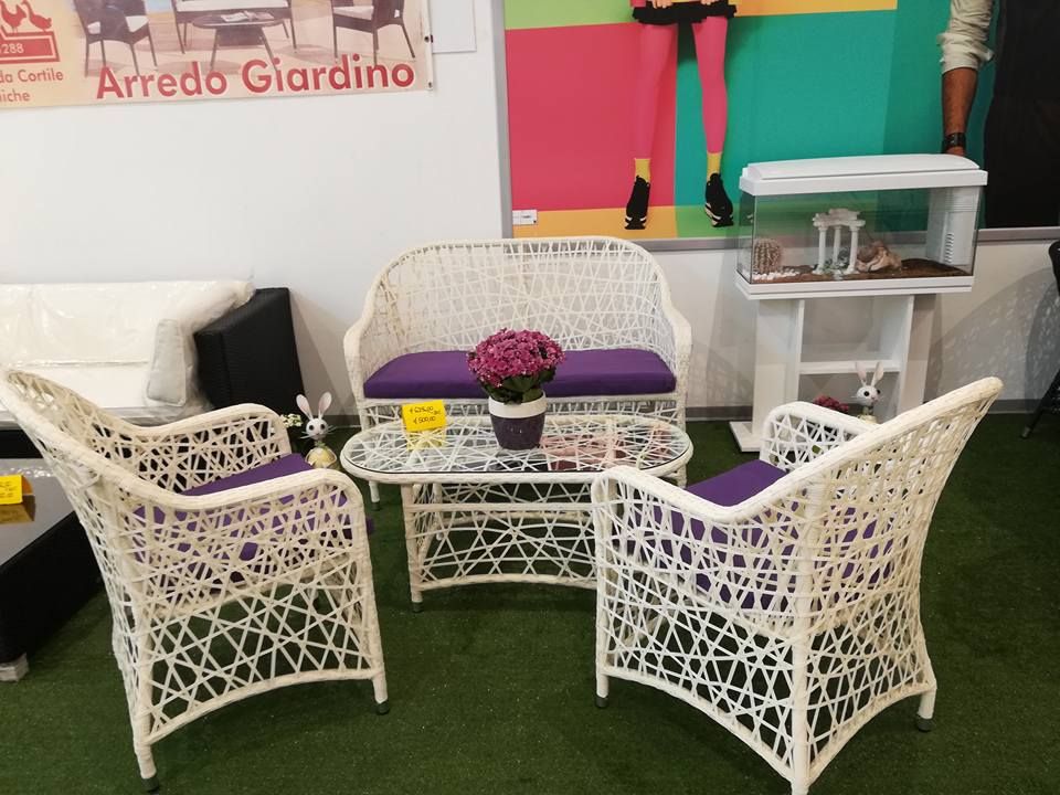 Set di mobili da esterno intrecciati bianchi con cuscini viola, tavolino e pianta in vaso.