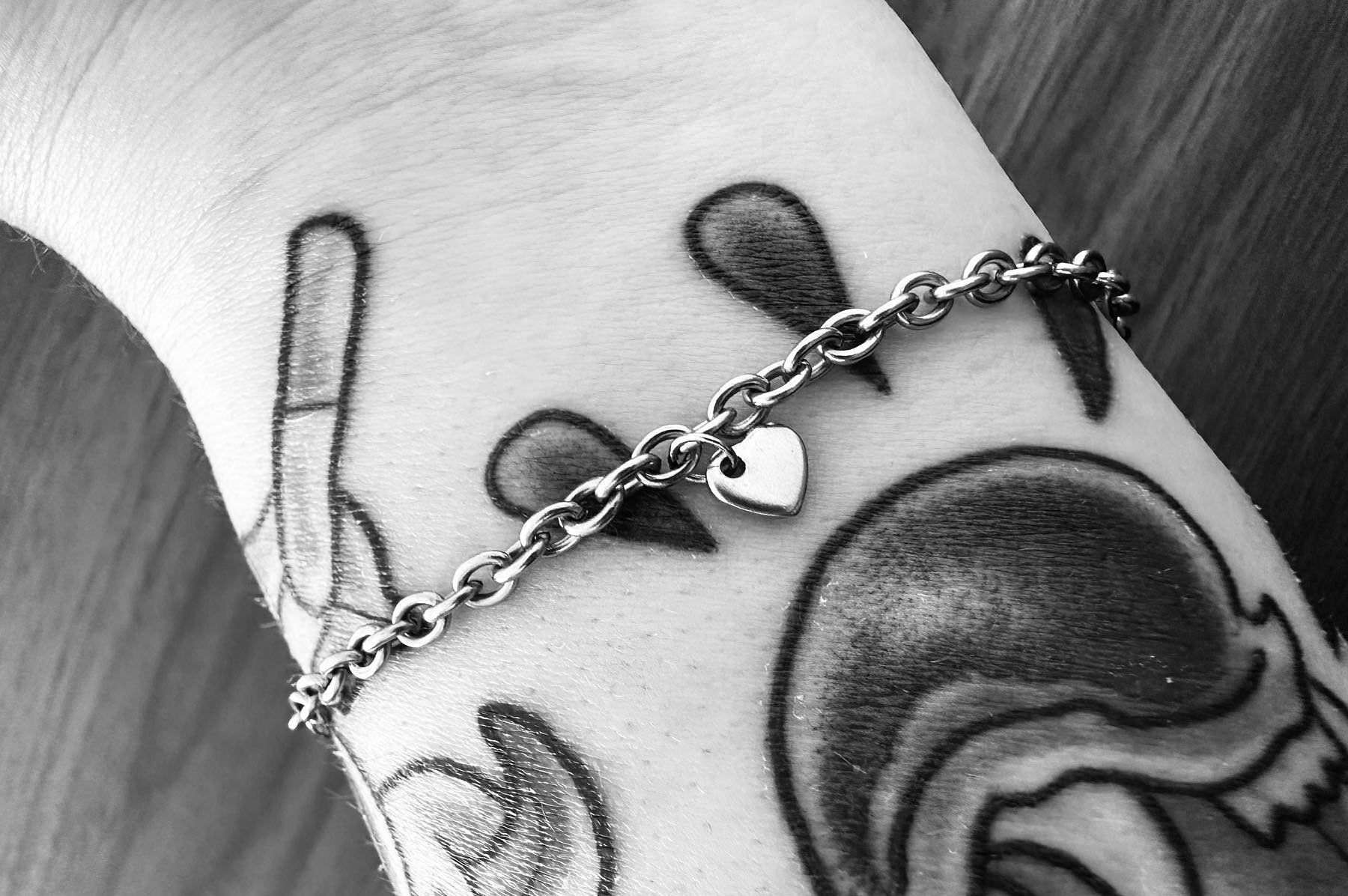 Close-up of a wrist with multiple tattoos and a silver chain bracelet with a heart charm.