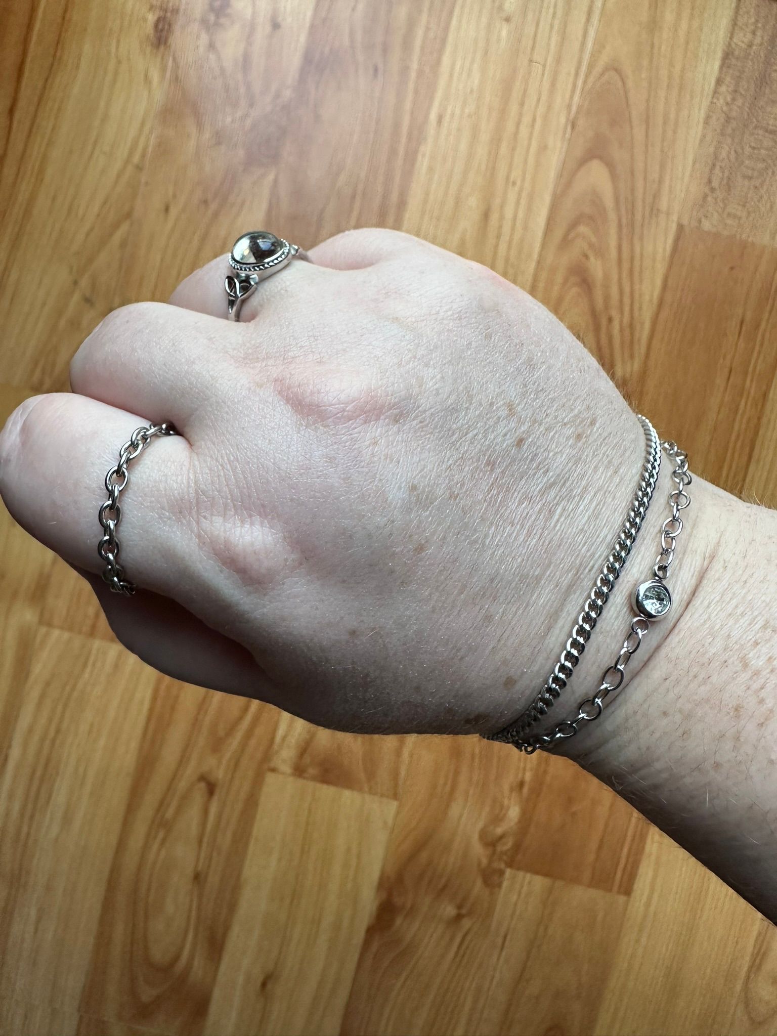 Hand with rings and bracelets on a wood-grain surface.