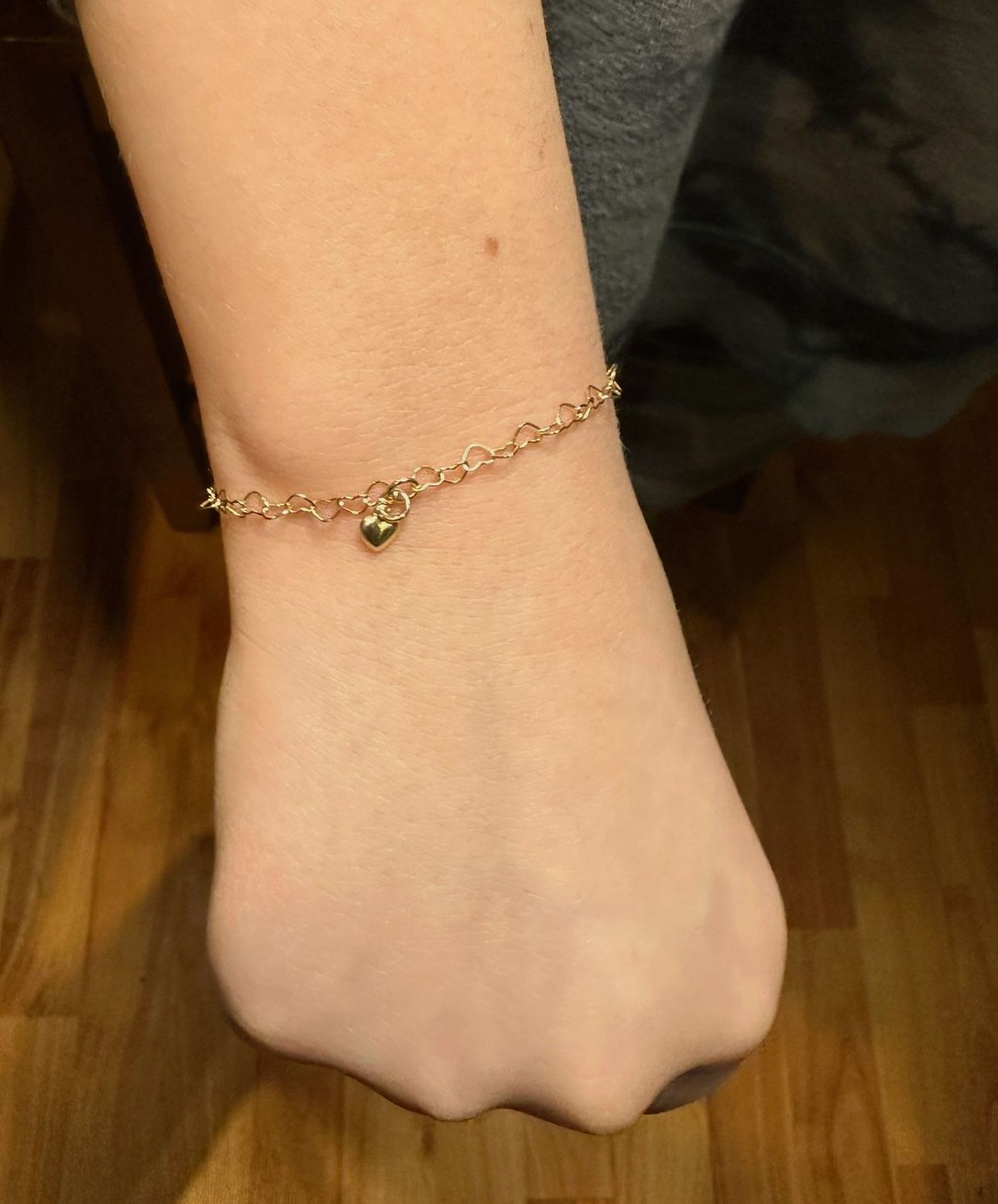 A gold chain bracelet with a heart charm on a wrist.