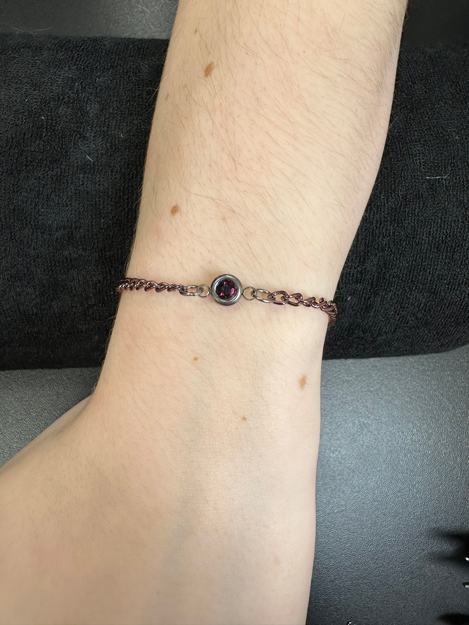 Wrist with a delicate bracelet, featuring small red beads and a central dark purple gem.