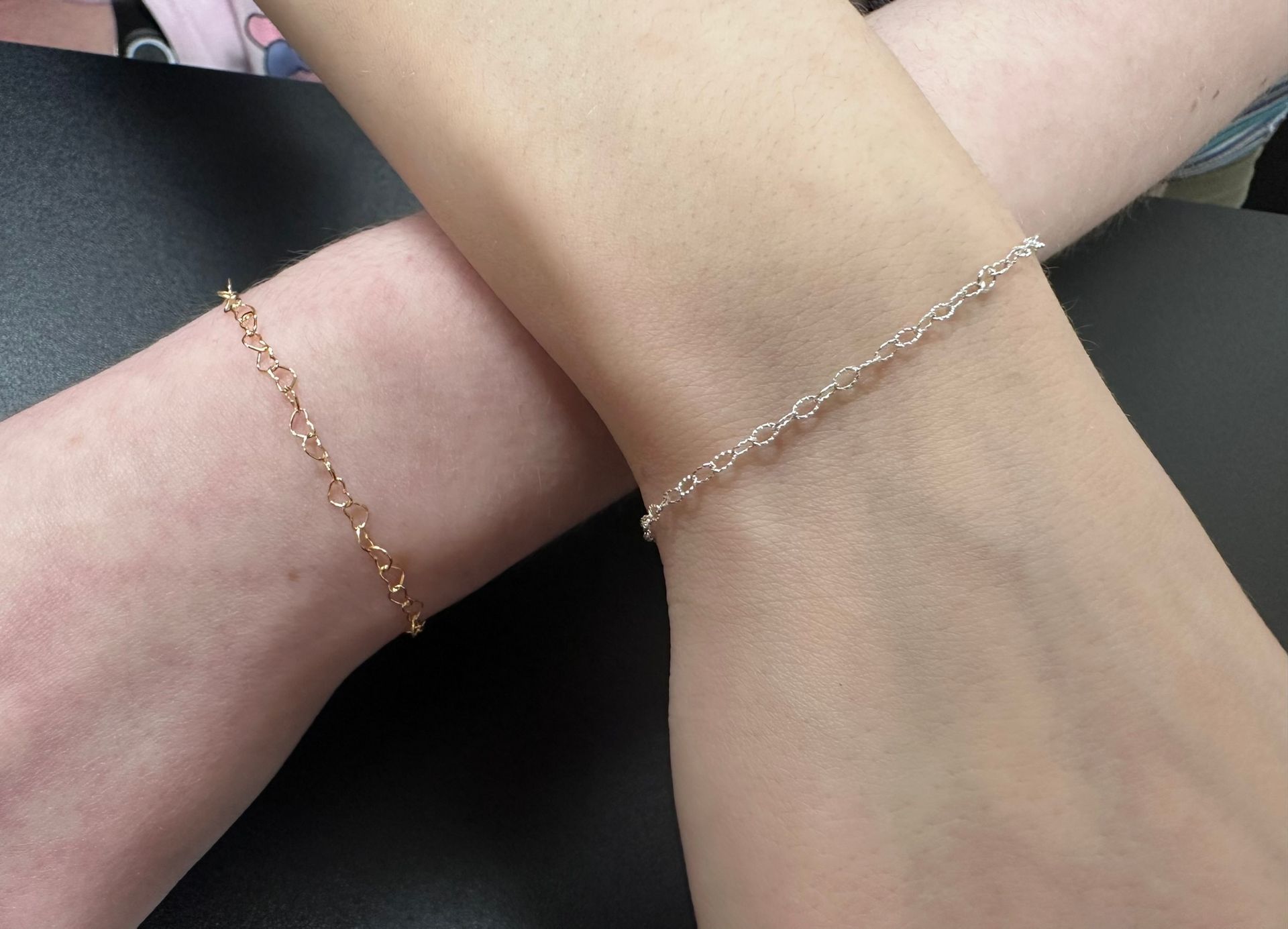 Two wrists, each with a gold chain bracelet, crossing.