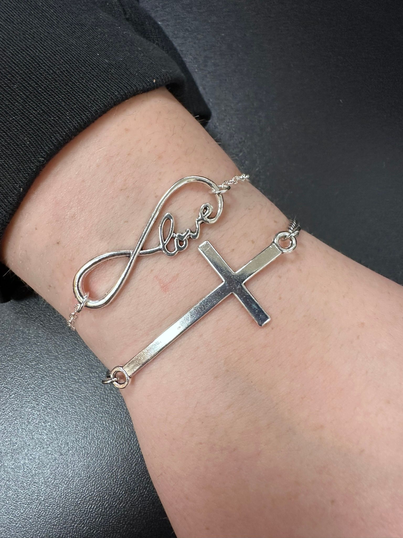 Silver bracelets with infinity symbol and cross on a wrist.
