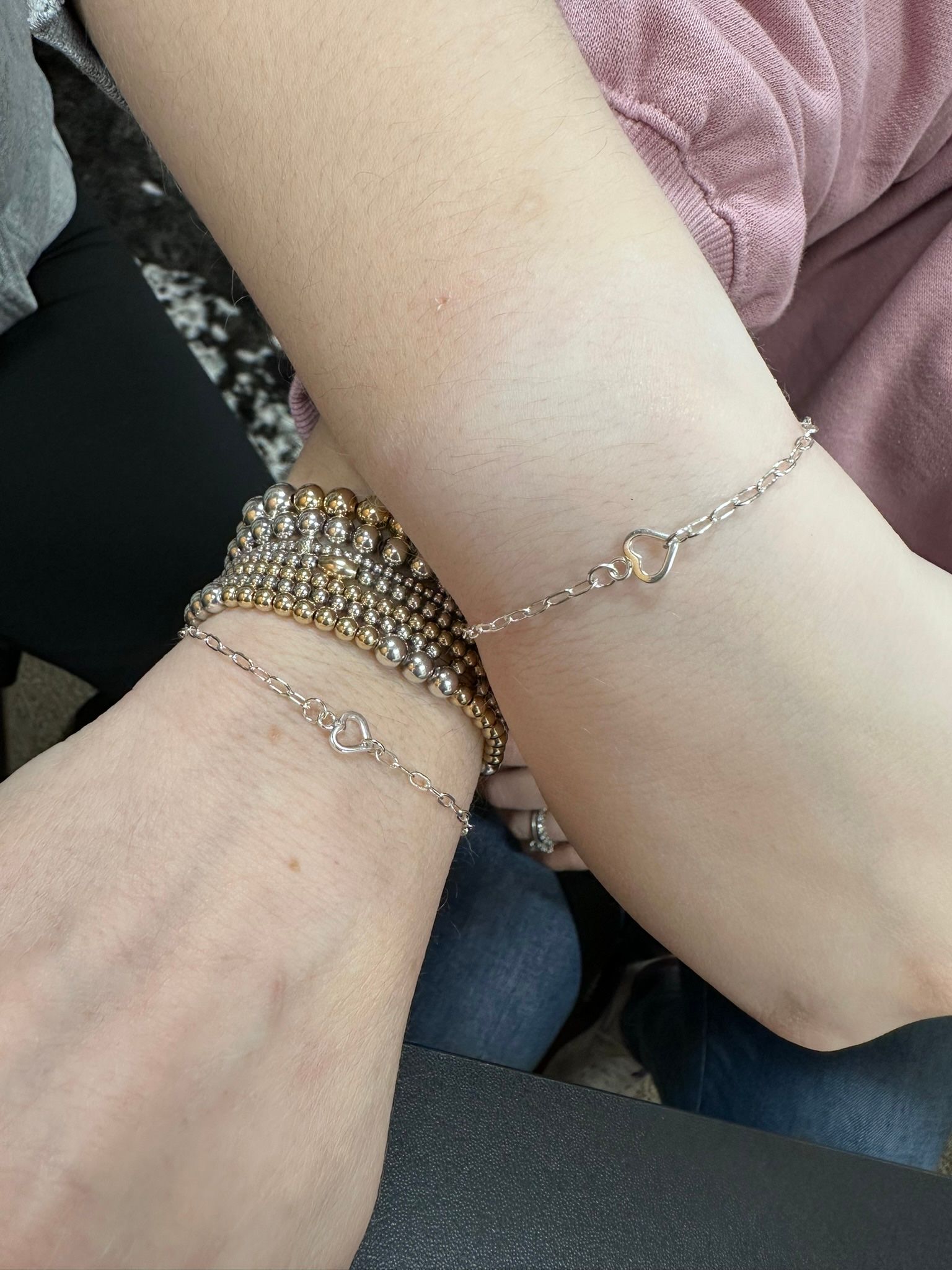 Two arms wearing bracelets are touching, the person on the left wearing a beaded bracelet.