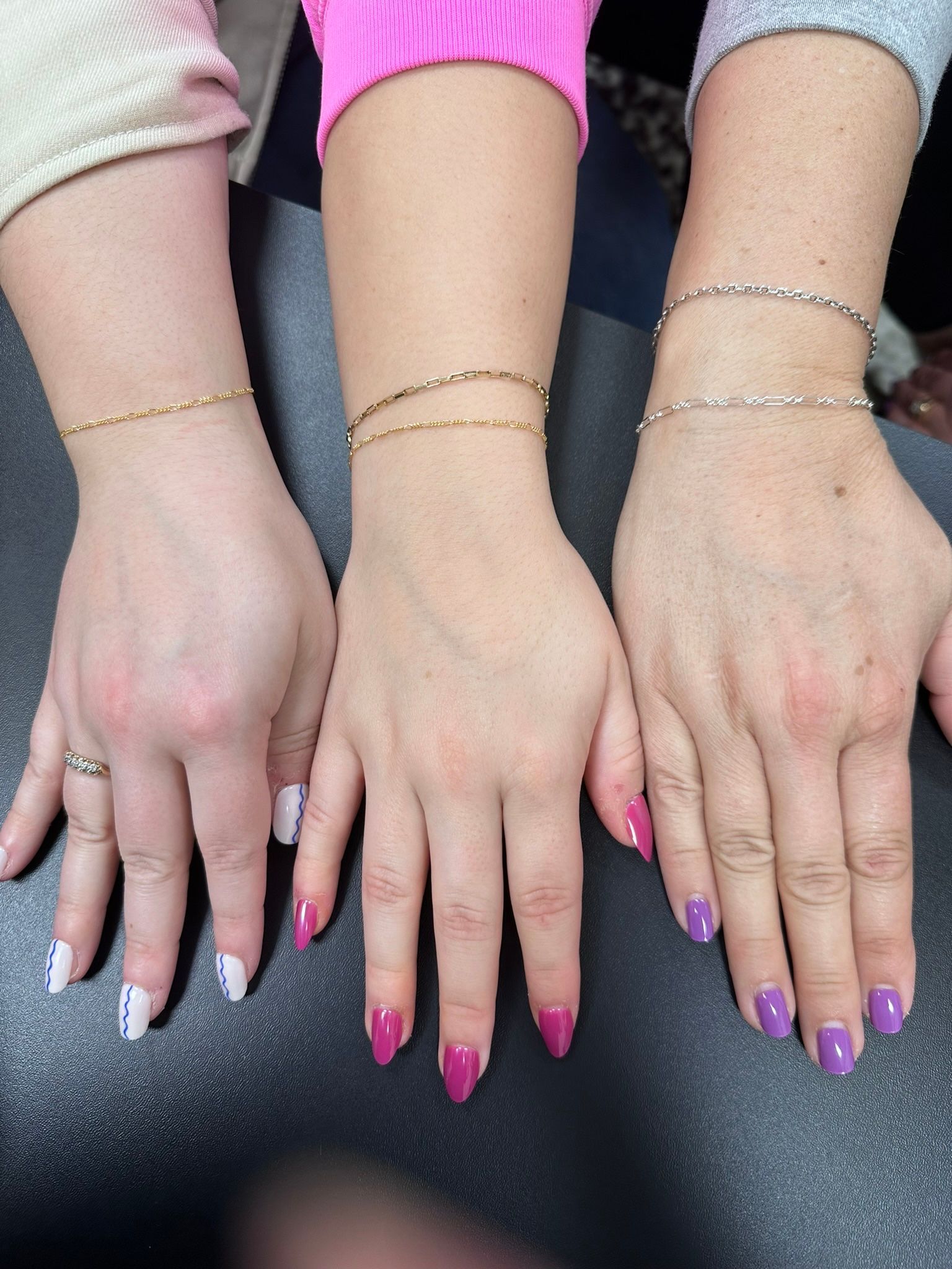Three hands with manicured nails and gold bracelets.