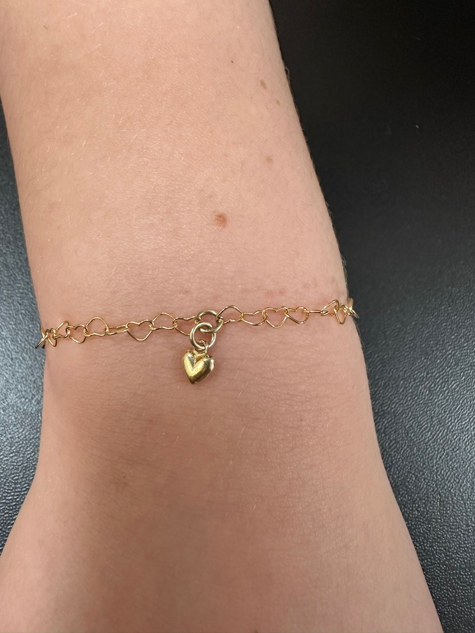 Gold bracelet with small hearts on wrist, a single heart charm hangs in the center.