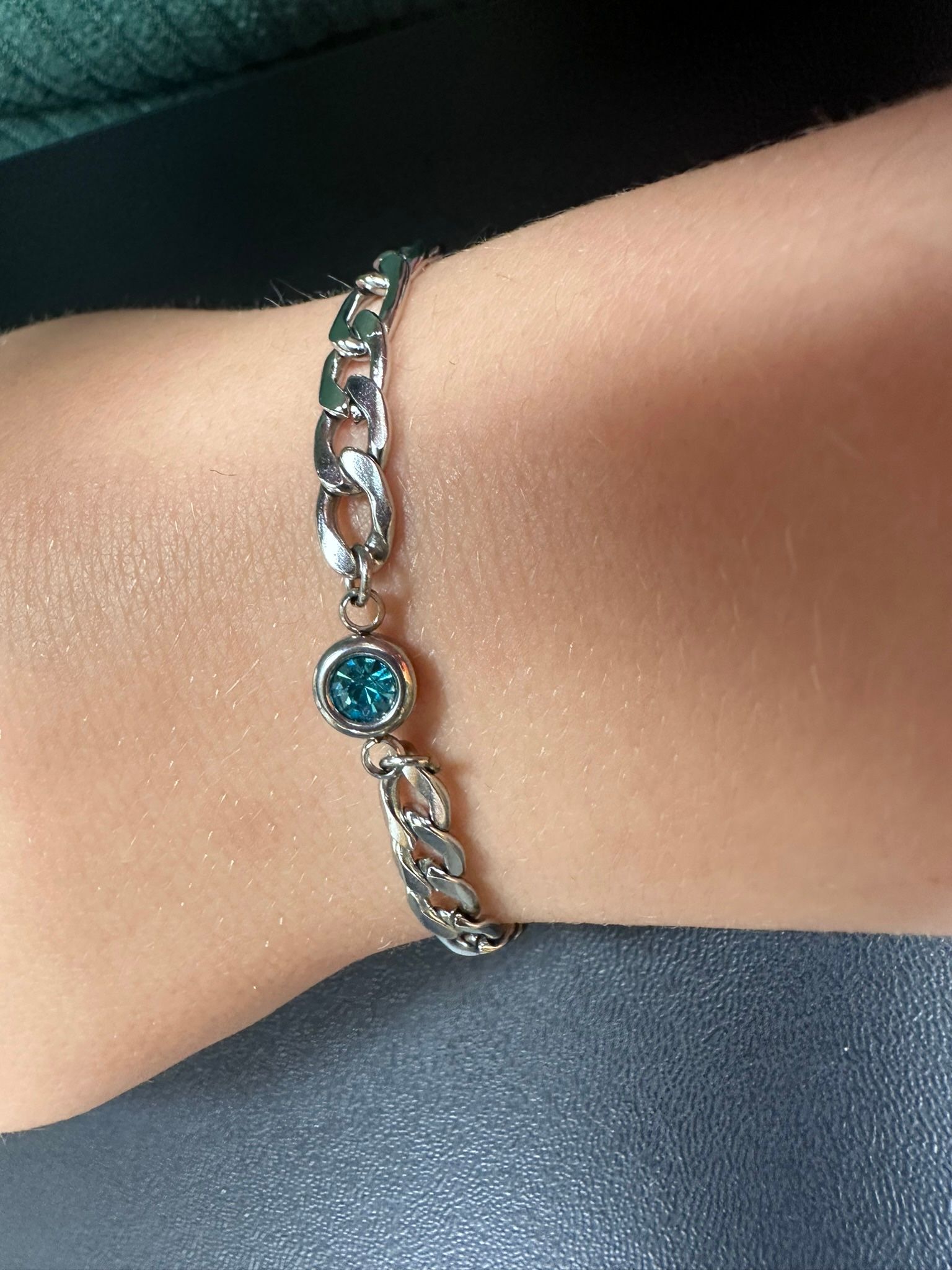 Silver chain bracelet with a teal-colored gemstone on a person's wrist.