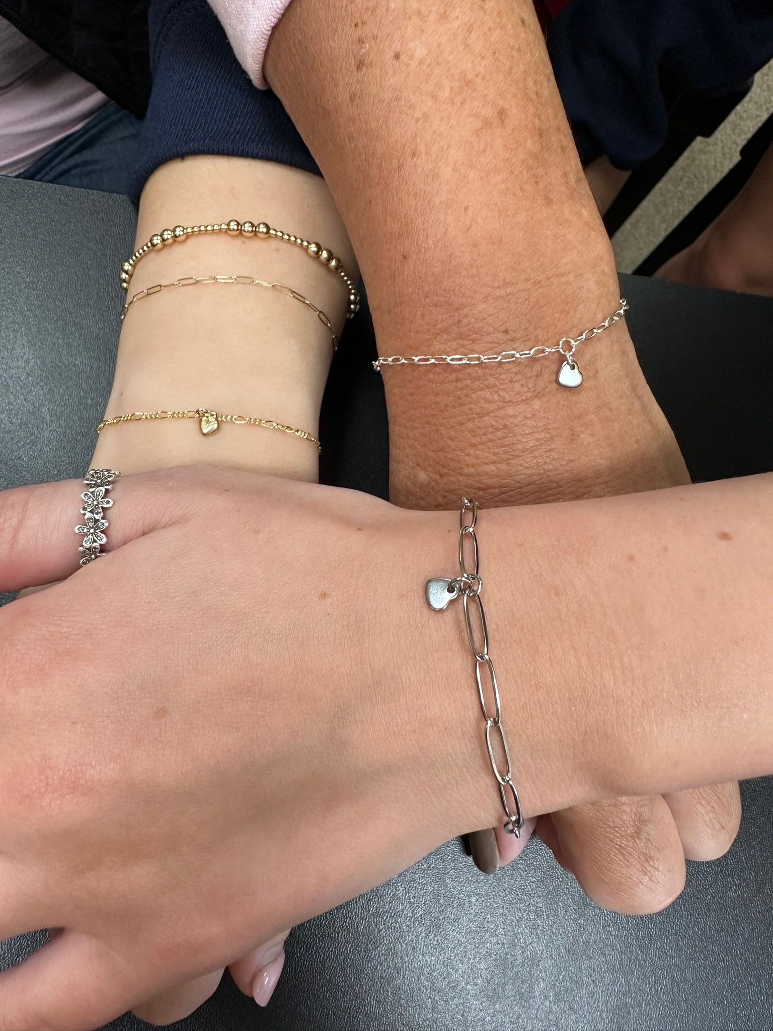 Three arms, varying skin tones, wearing bracelets. Hands are clasped together.