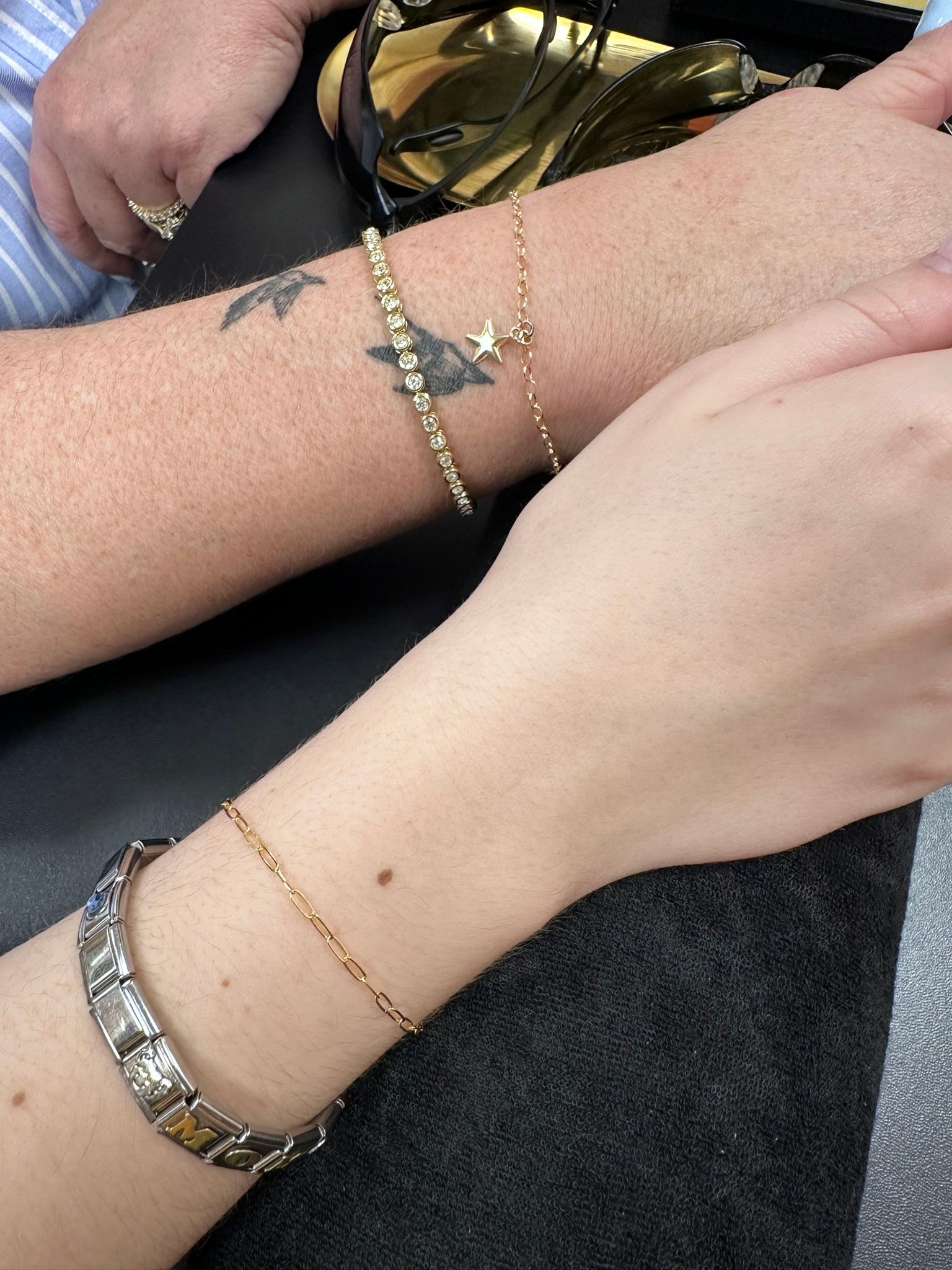 Two wrists with bracelets; one with a tattoo of a bird and star.