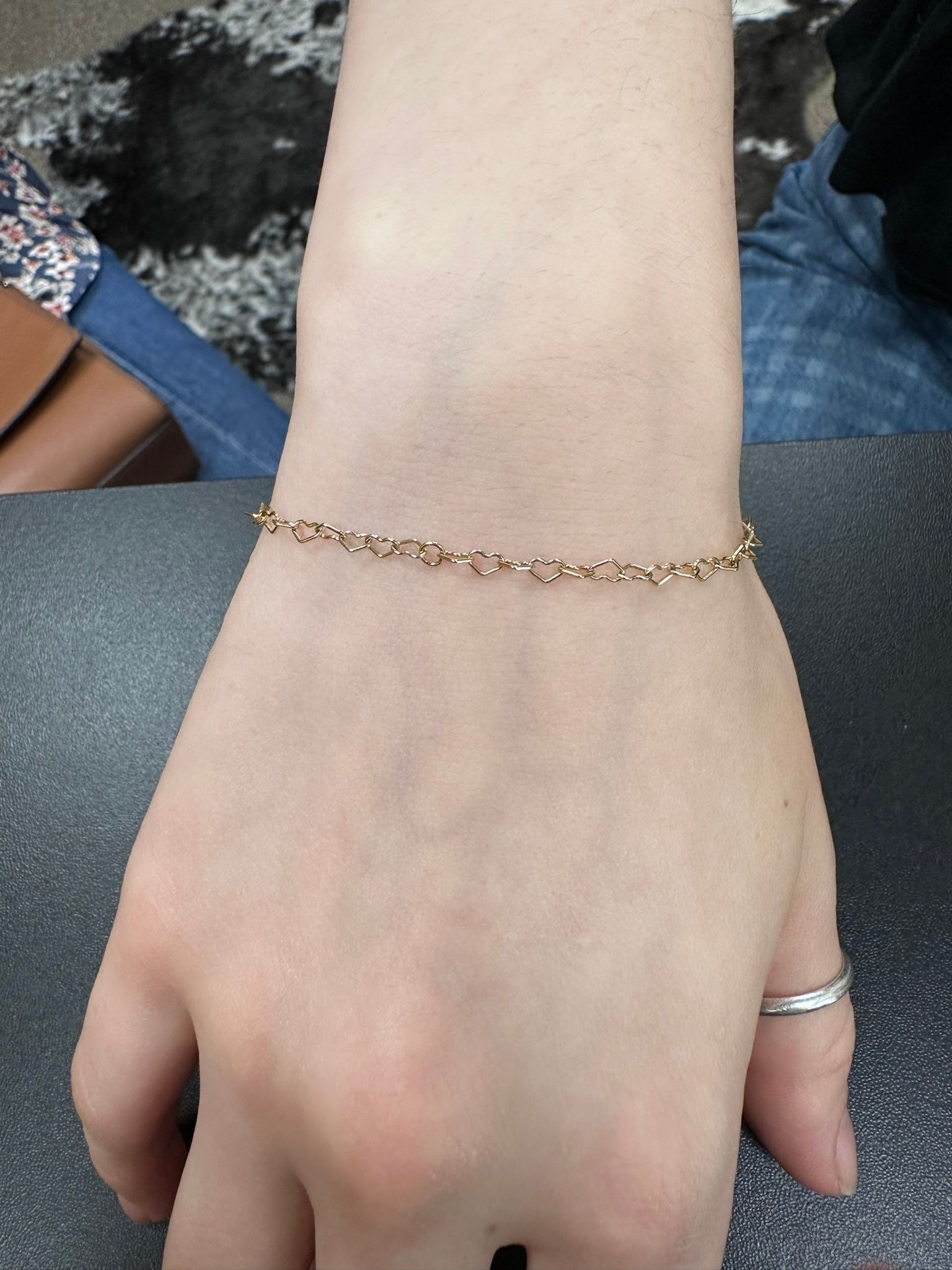 Hand with a gold chain bracelet and silver ring.