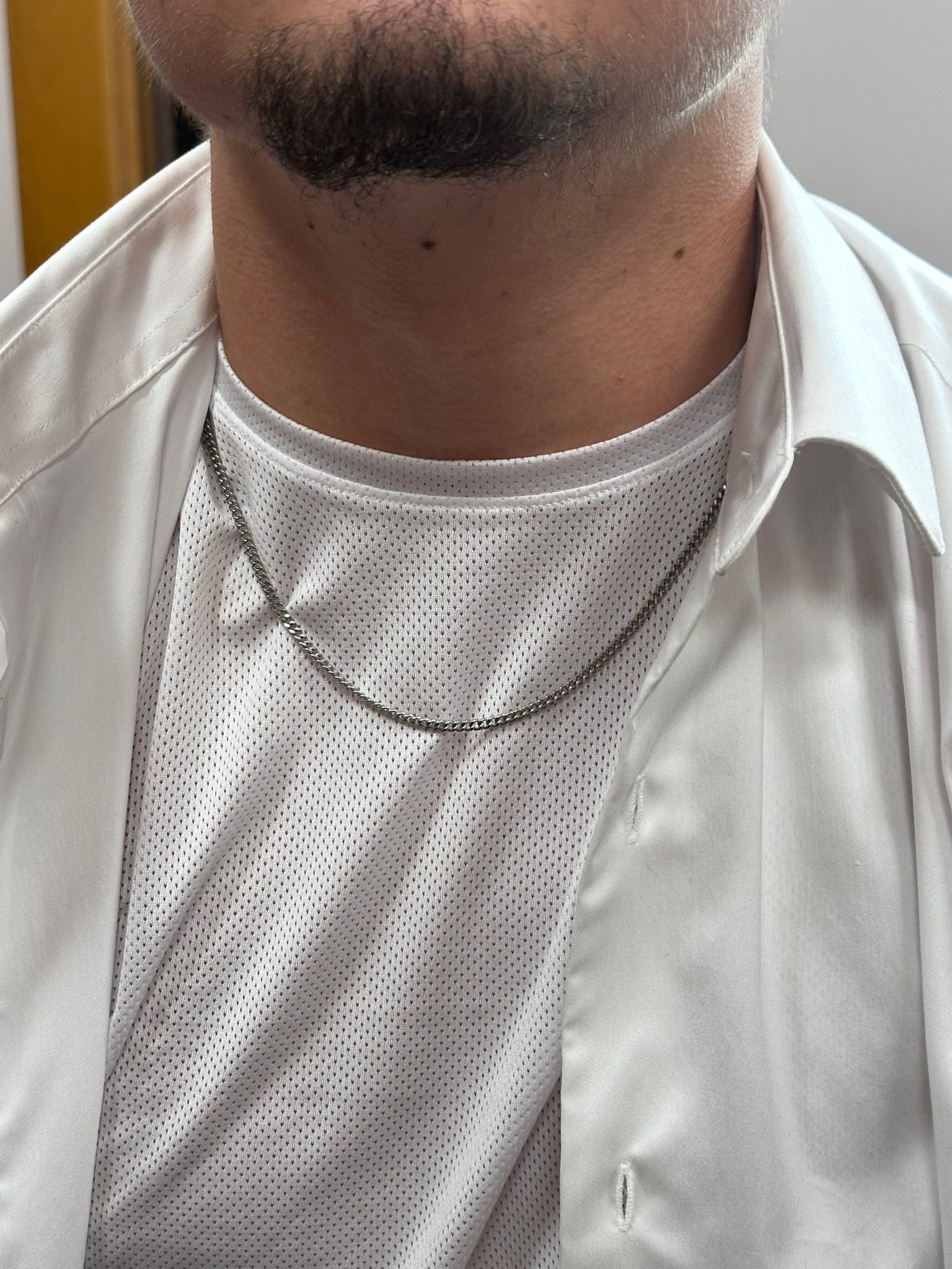 Man wearing a white shirt and a chain necklace, seen from the chest up.