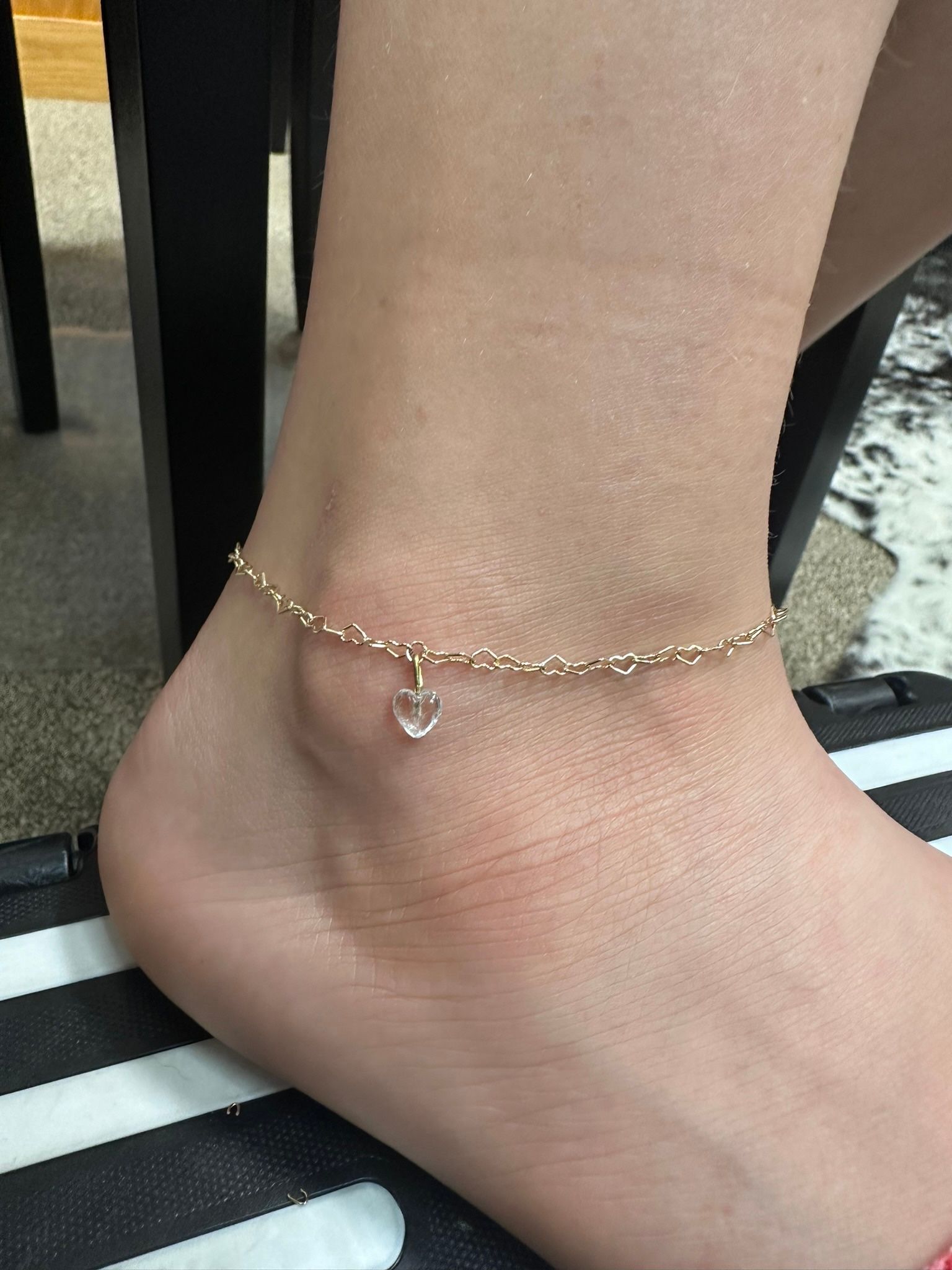 Ankle with a gold beaded anklet and a small heart charm.