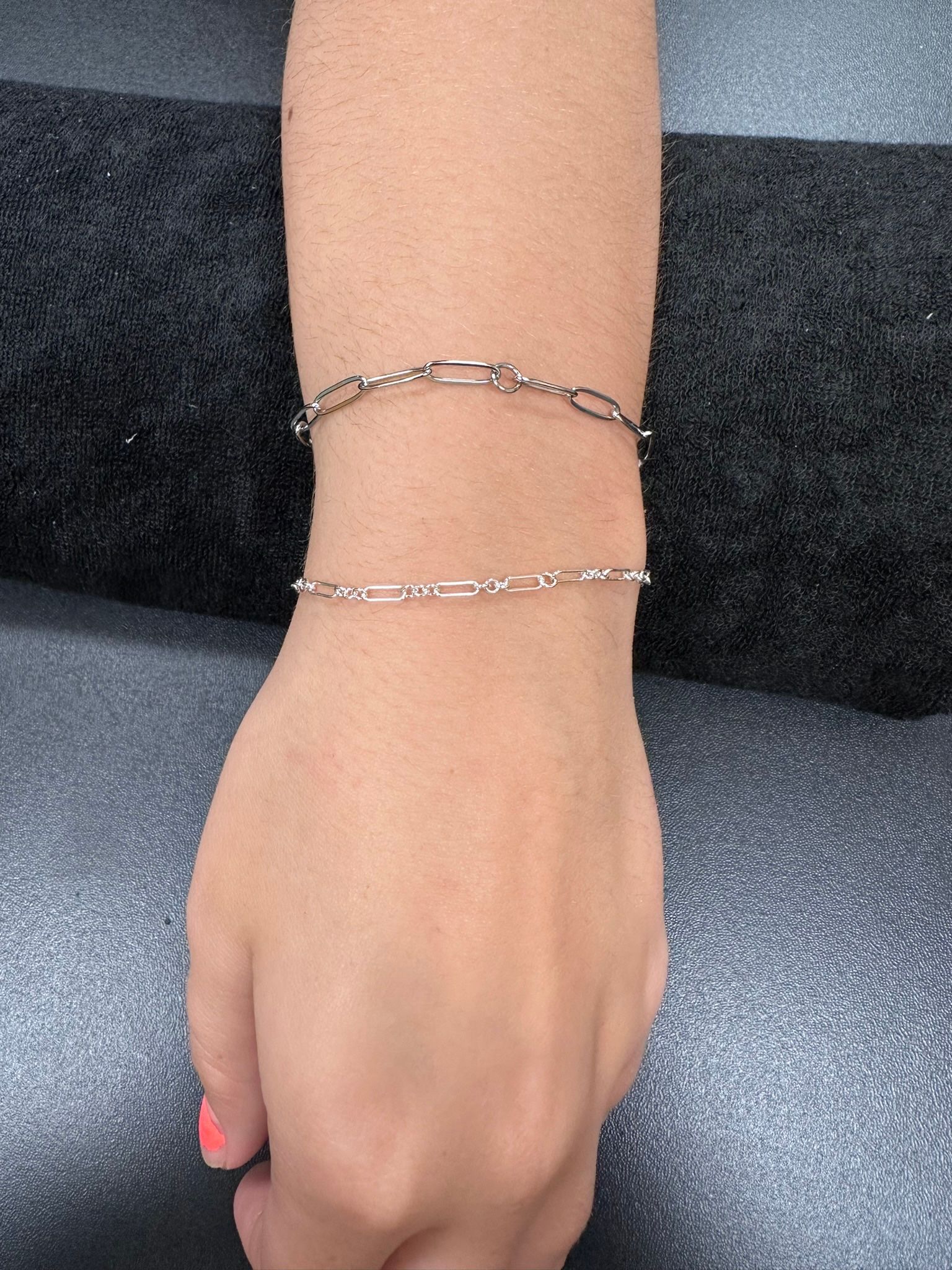 Two silver chain bracelets on a person's wrist against a dark background.