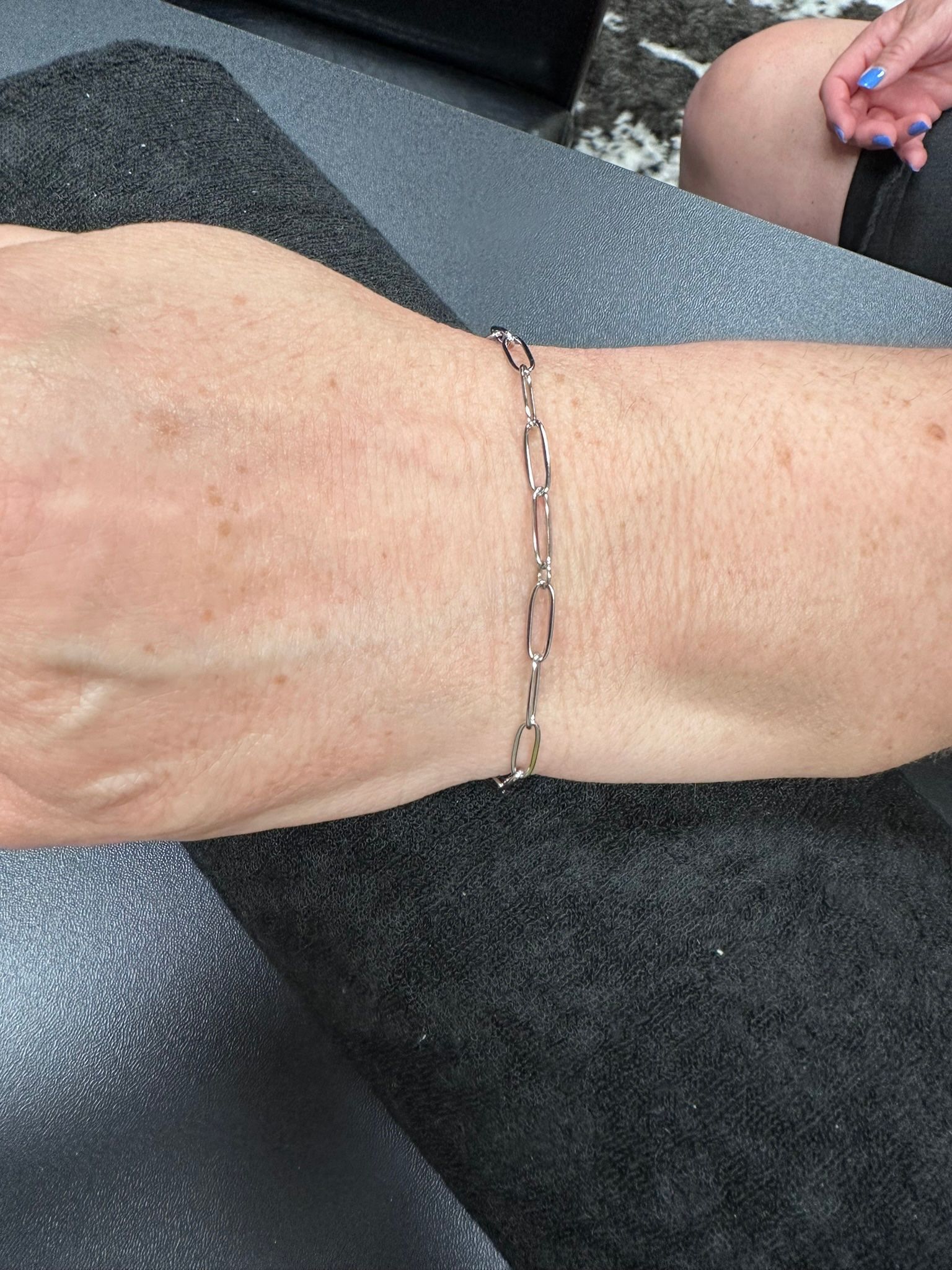 Silver link bracelet on a person's wrist, resting on a gray surface.