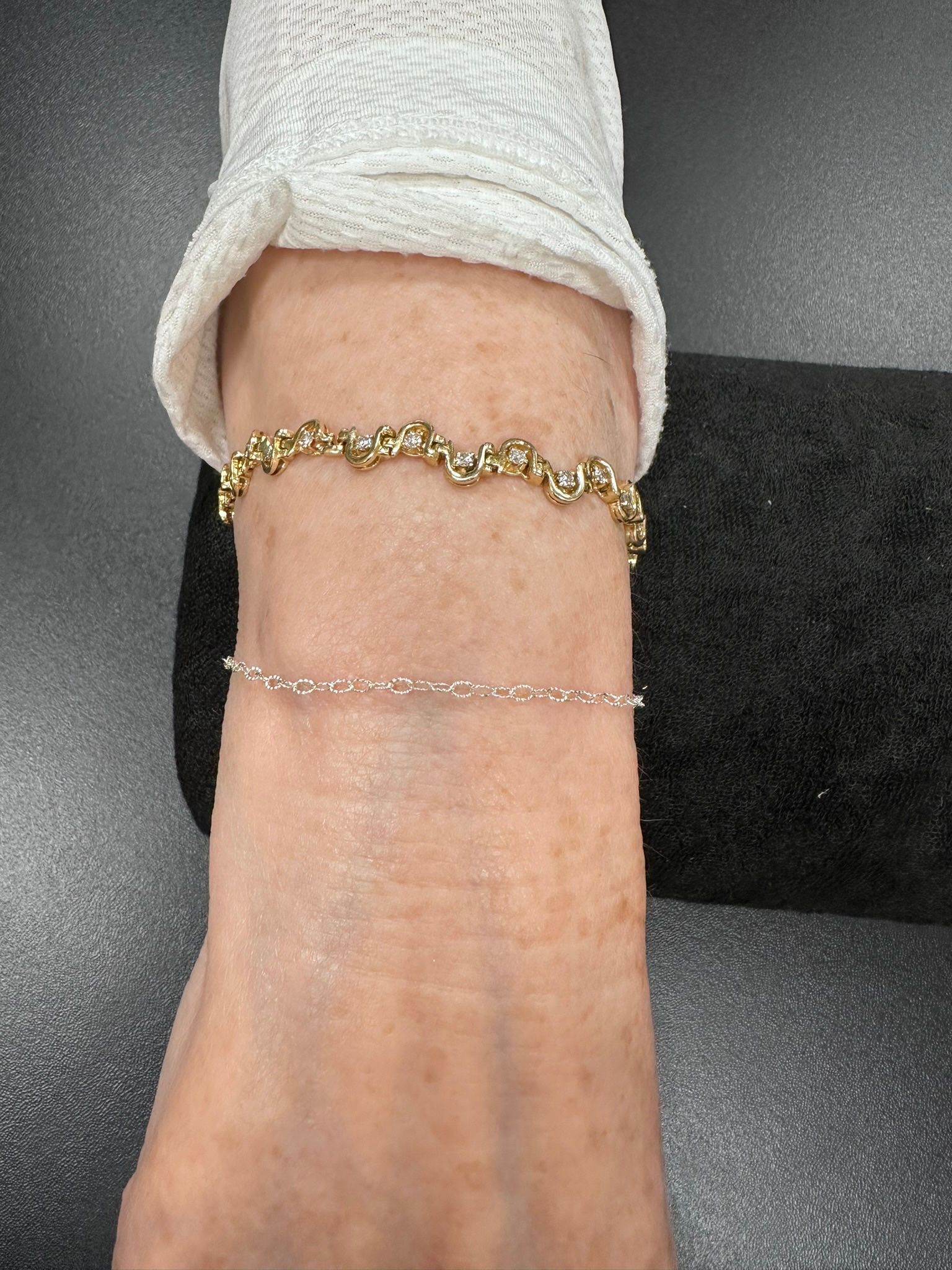 Wrist with two gold bracelets and a white sleeve.