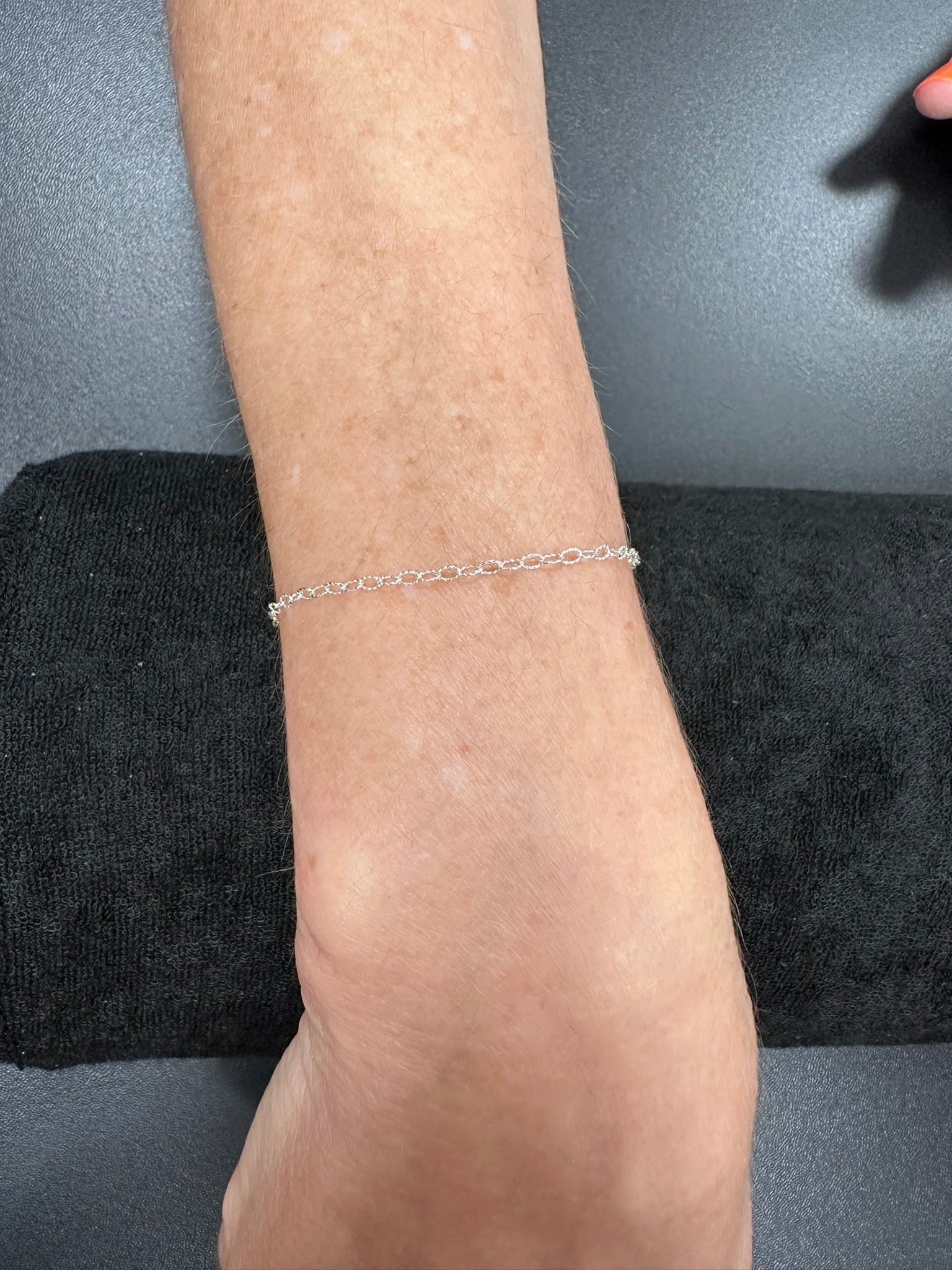 Wrist with silver chain bracelet on a black towel.