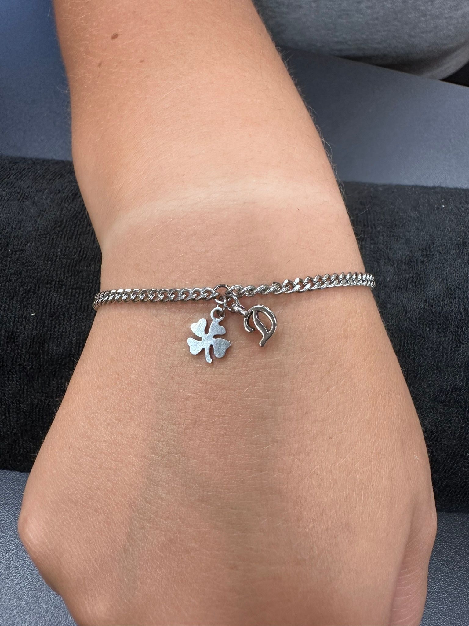 Silver bracelet with clover and heart charms on a wrist.