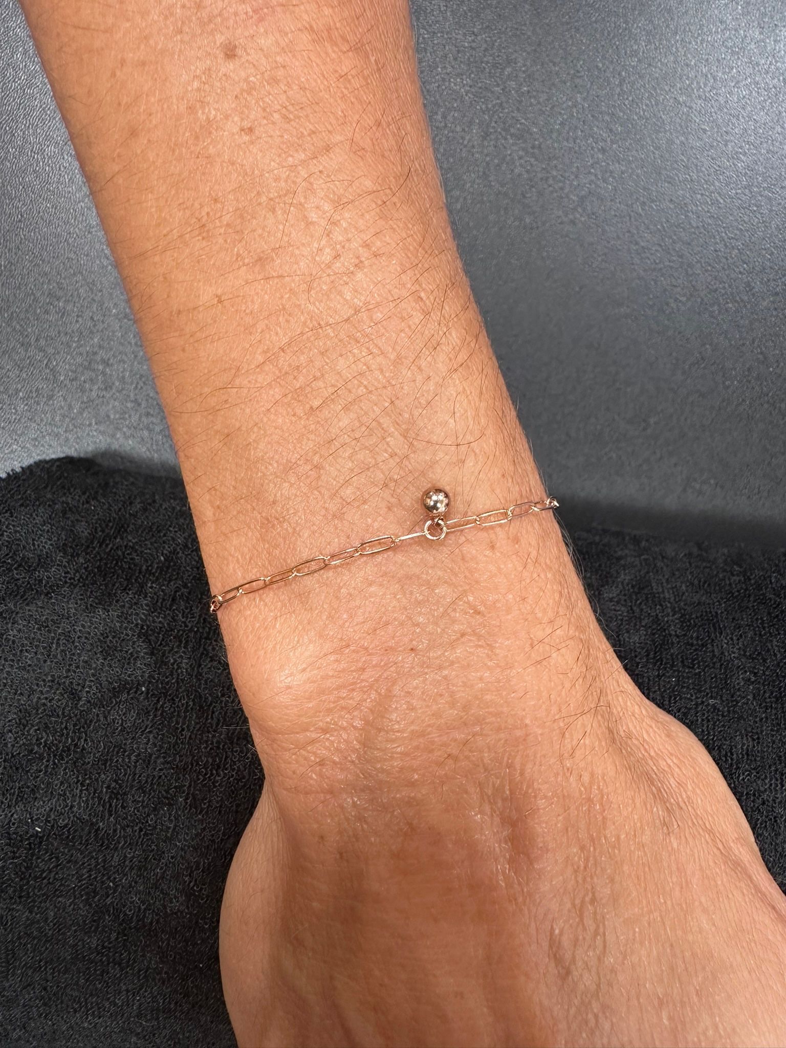 Close-up of a wrist with a delicate gold anklet with a small ball charm.