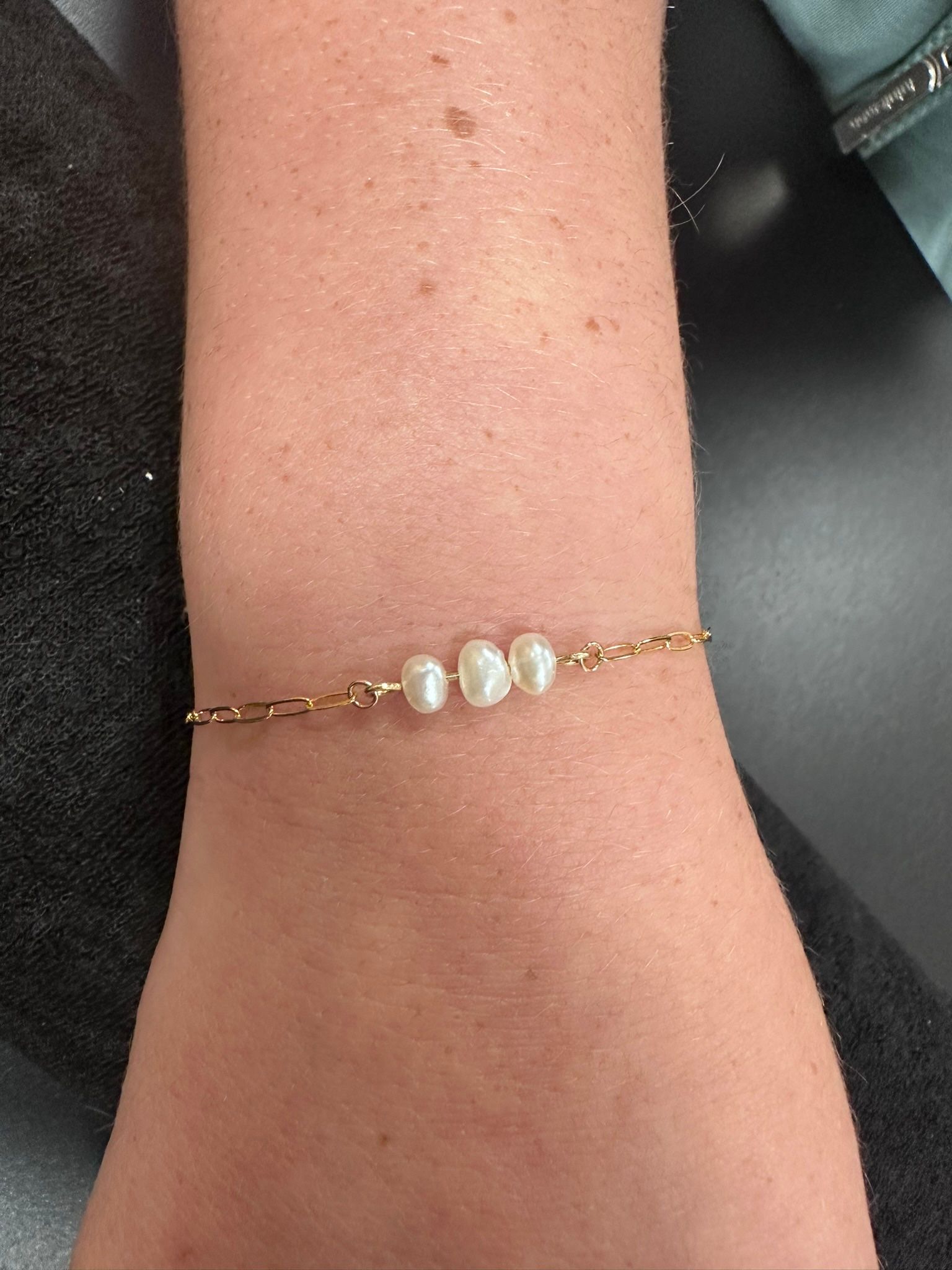 A gold bracelet with three white pearls on a wrist.