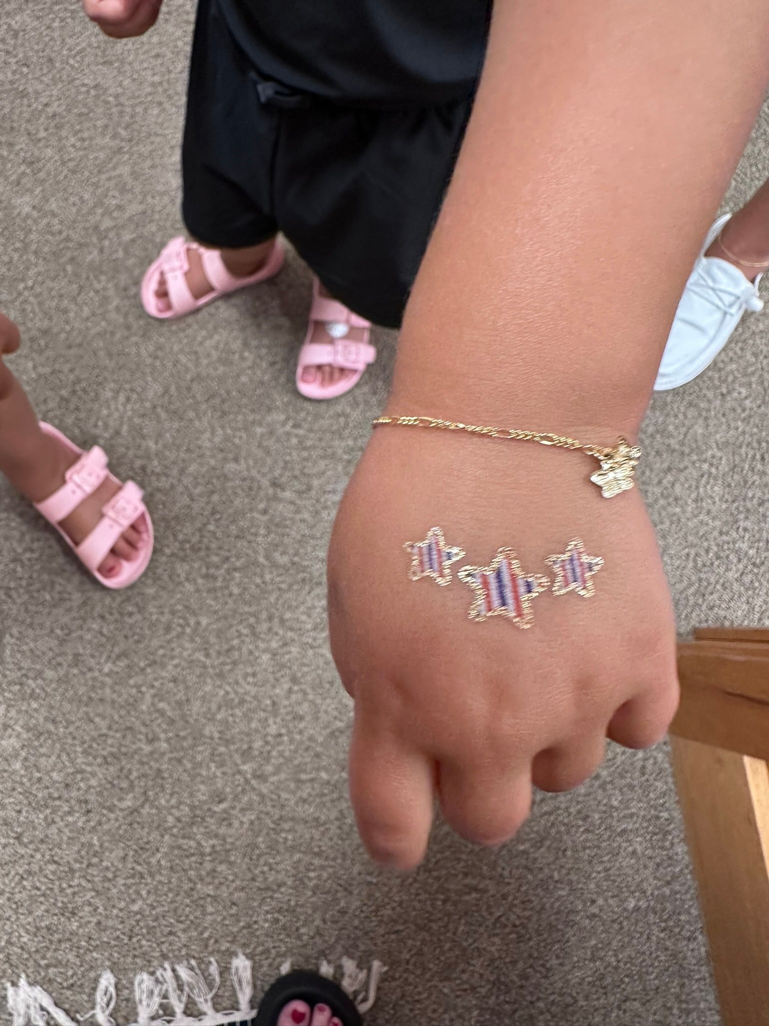 Child's hand with a temporary tattoo and a gold bracelet; feet in pink sandals visible.
