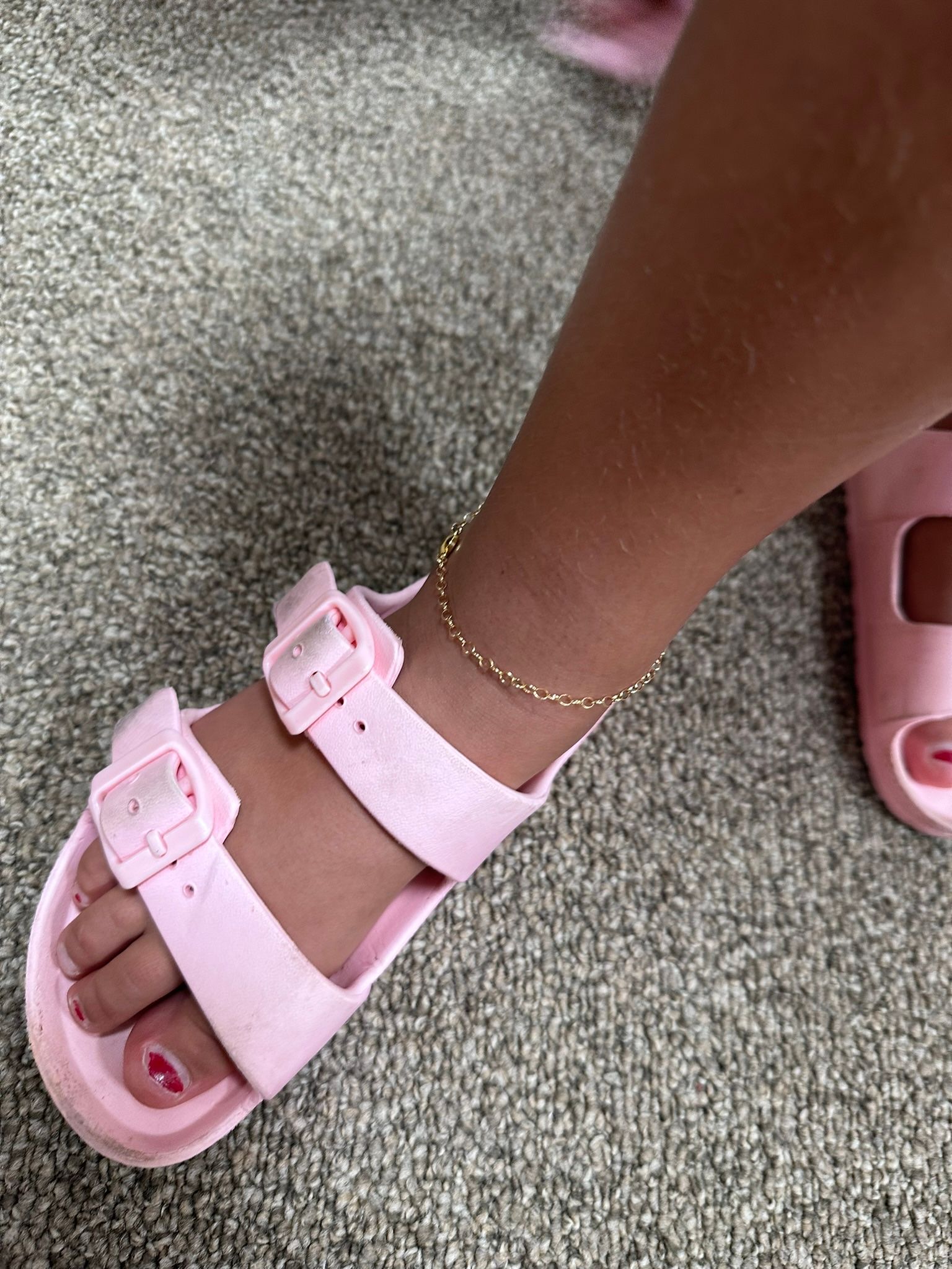 Pink sandals with two straps on a foot wearing a gold ankle bracelet.
