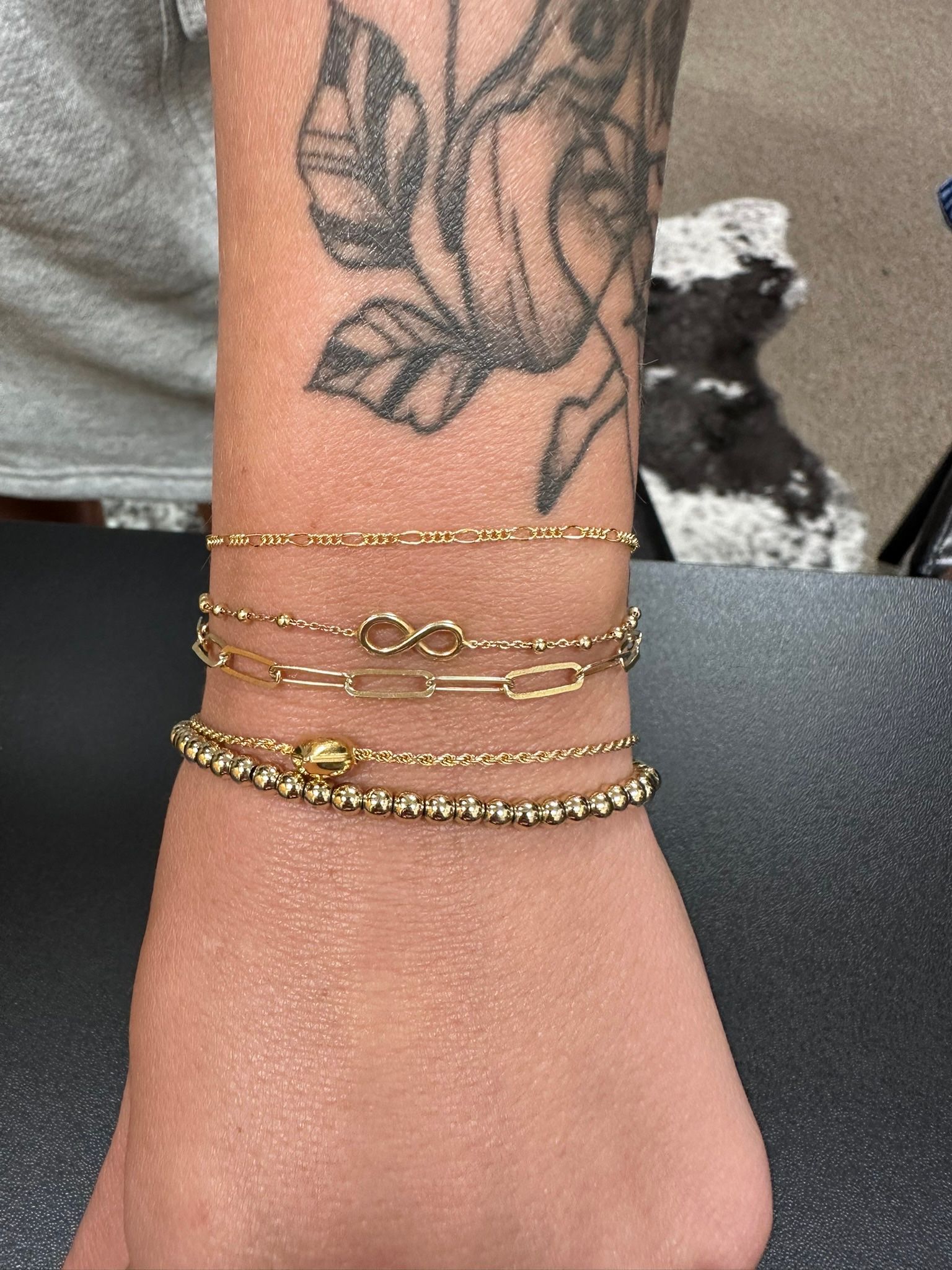 A wrist with four gold bracelets, and a floral tattoo on the arm.