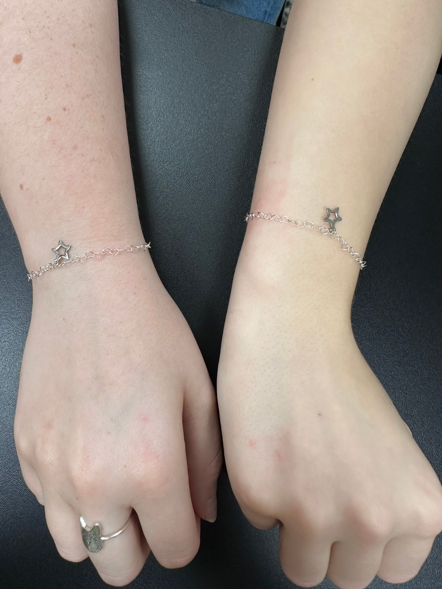 Two wrists with silver bracelets, each with a small star charm, held up side by side.