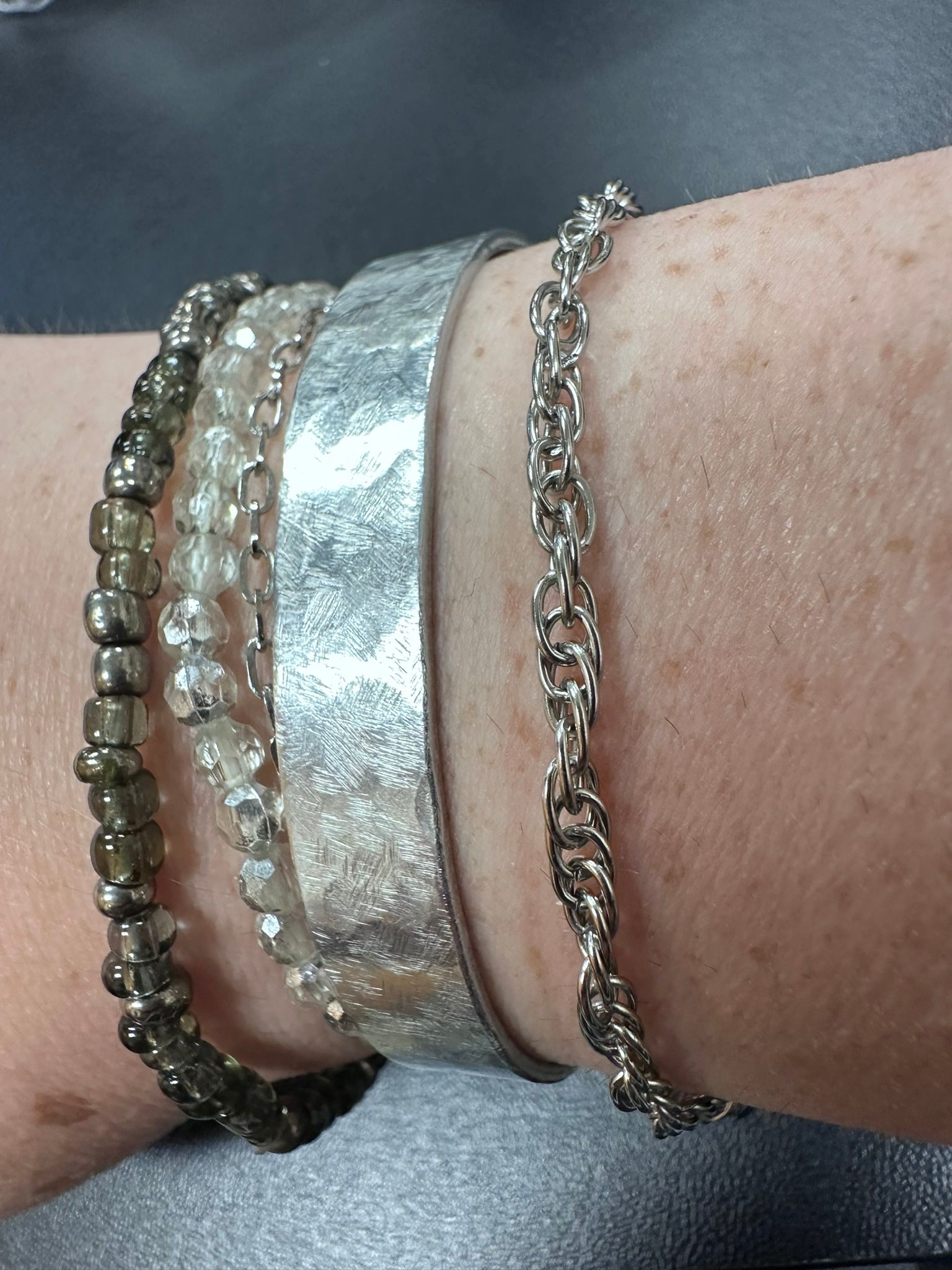 Four silver bracelets on a wrist: beaded, chain-link, and textured metal.