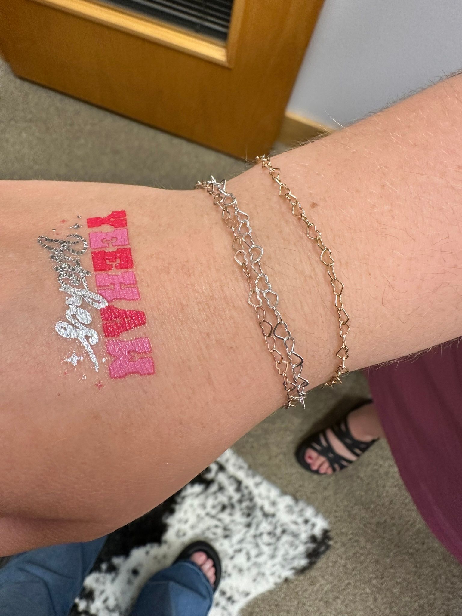 Arm with temporary glitter tattoos of teddy bears and silver glitter; gold bracelet.