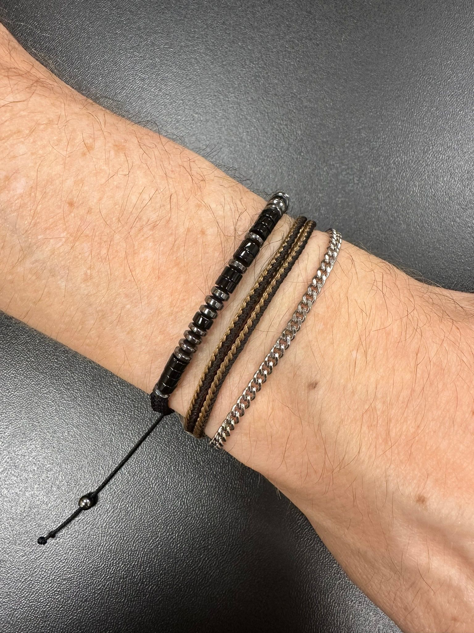 Wrist with four stacked bracelets, black, brown, and silver beaded and chain styles.