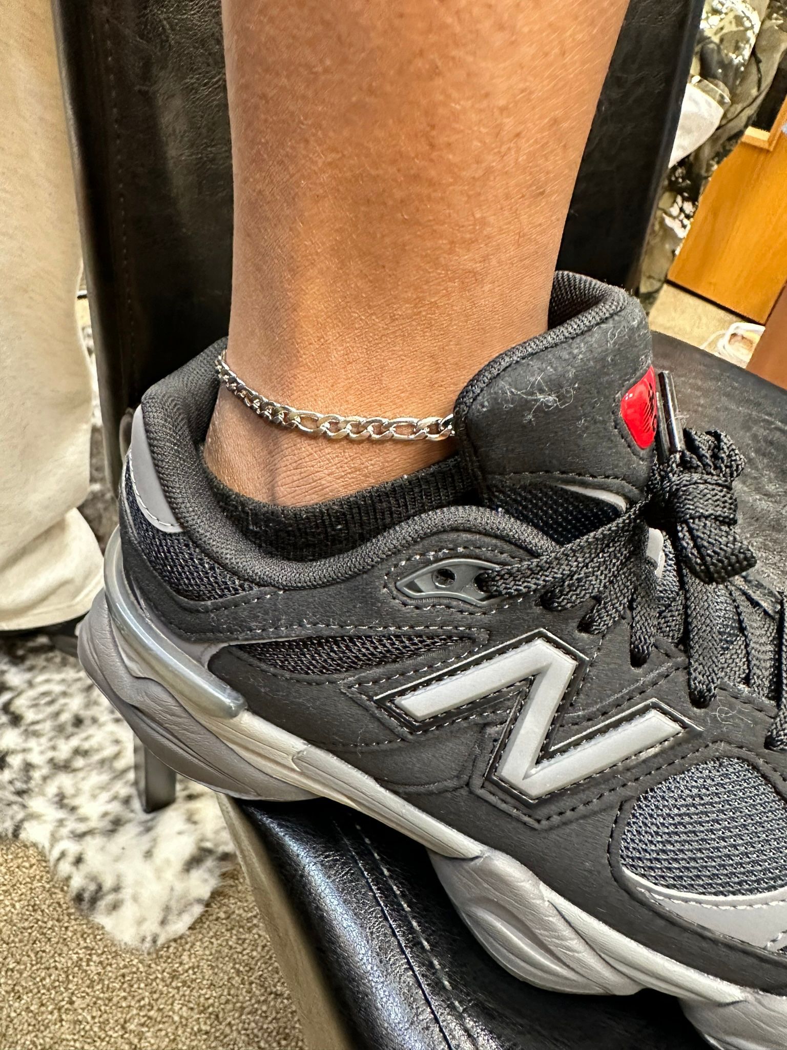 Black sneaker with silver details and an ankle bracelet on a foot.