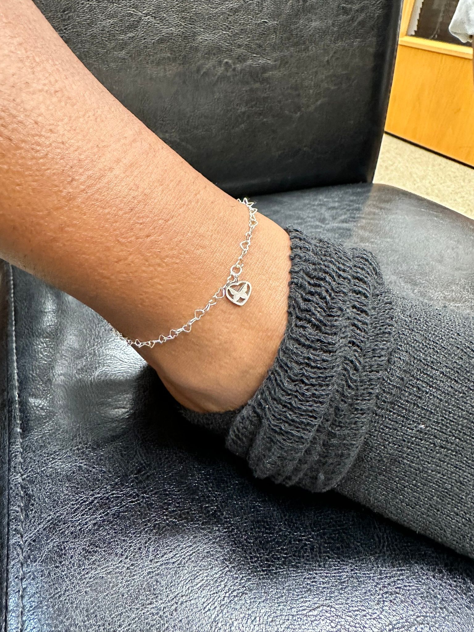 Anklet with a charm on a person's ankle over a dark sock.