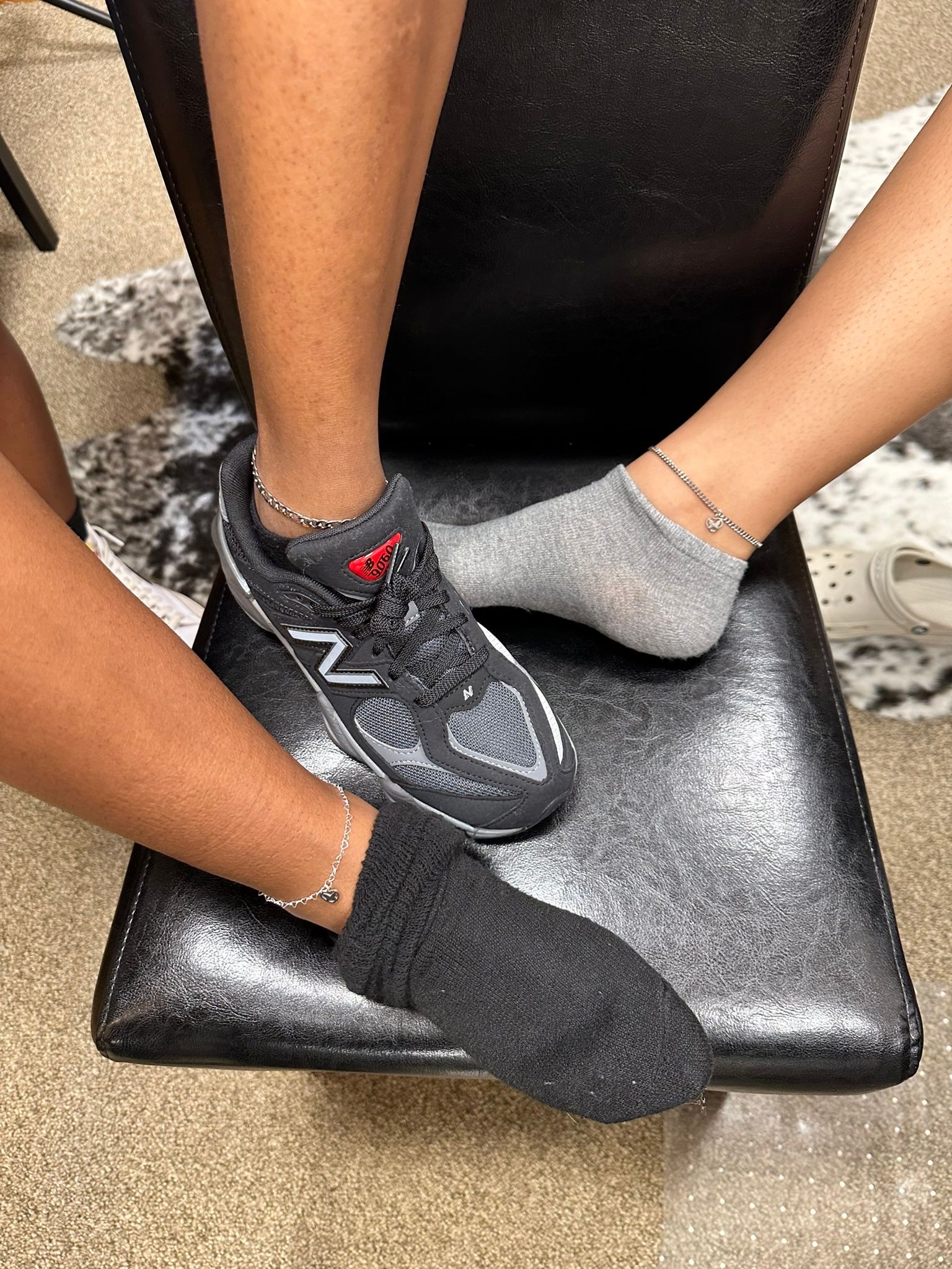 Three feet: one in a sneaker, two in socks, resting on a black glitter chair.