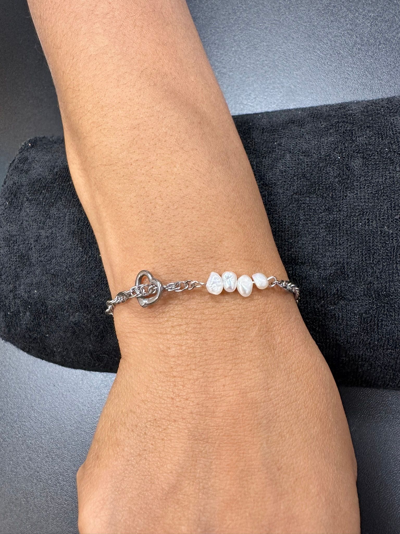 Silver bracelet with heart charm and white beads on a person's wrist.